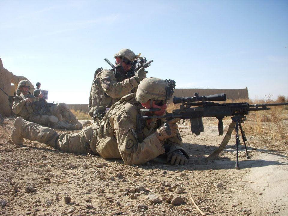 Soldiers in desert camouflage lying on ground, aiming rifles with scopes, in a desert environment.