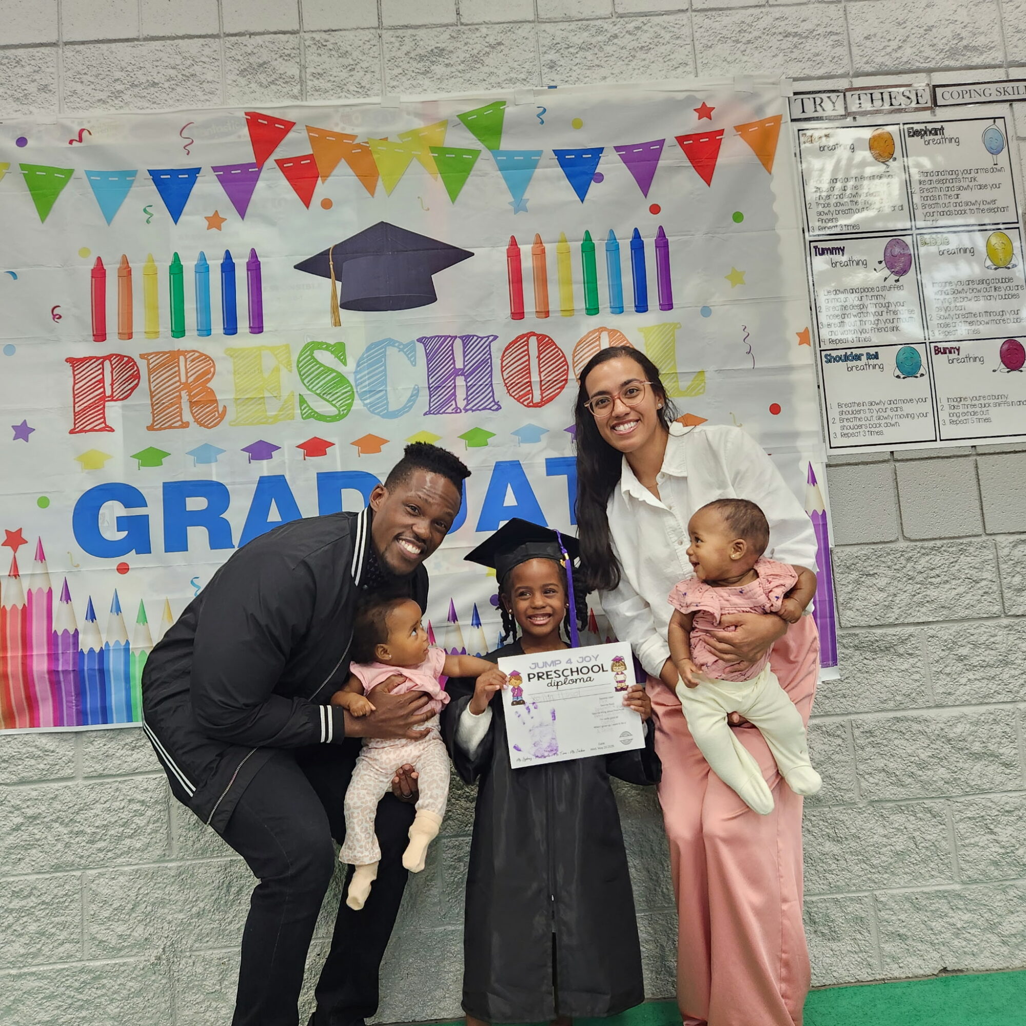 Group of four people celebrating graduation, with a colorful banner and children, one holding a certificate.
