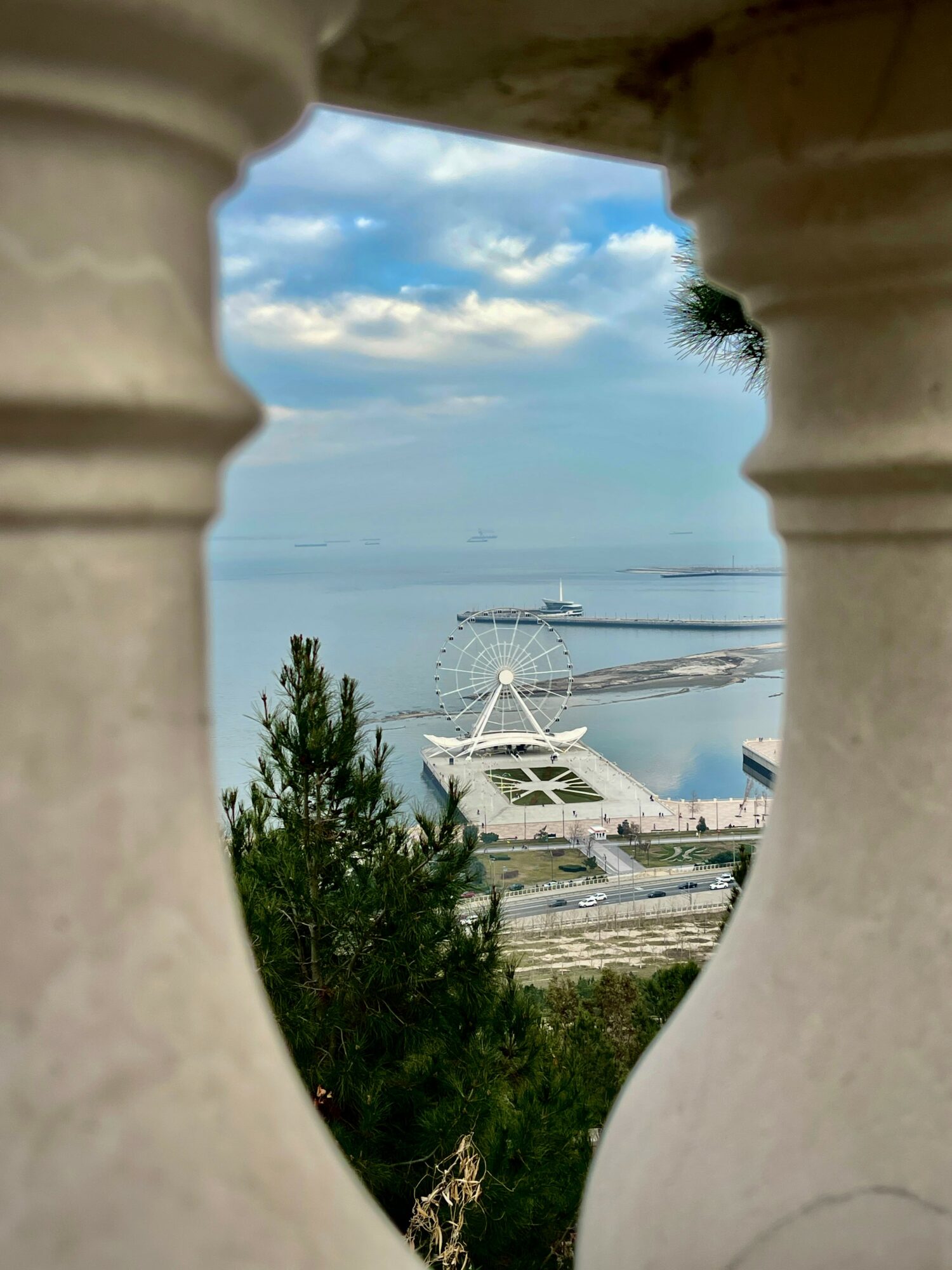 View of a marina with boats, seen through a stone balustrade, with a cloudy sky and water in the background.