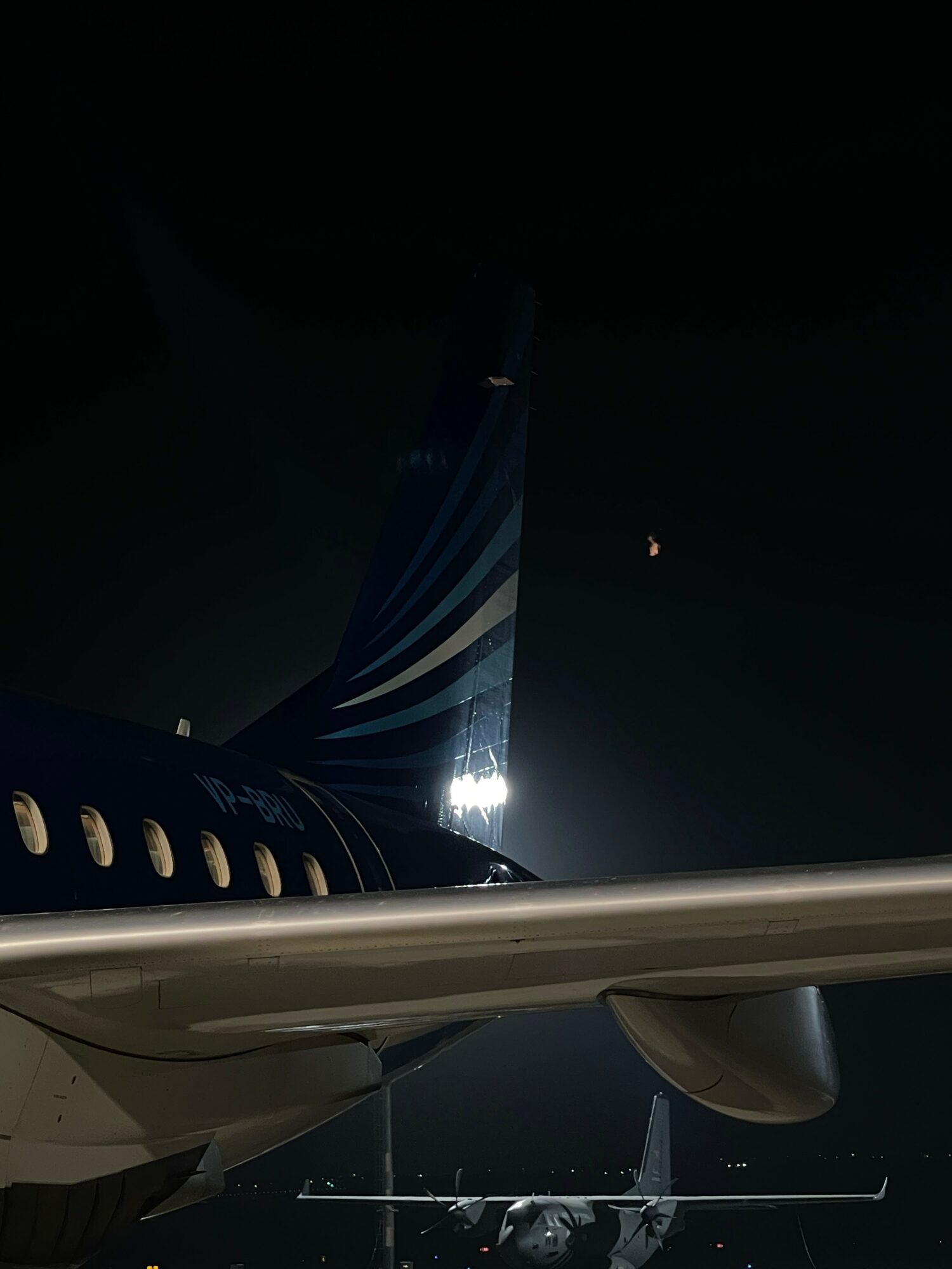 Nighttime view of an airplane wing and tail with a dark sky background.