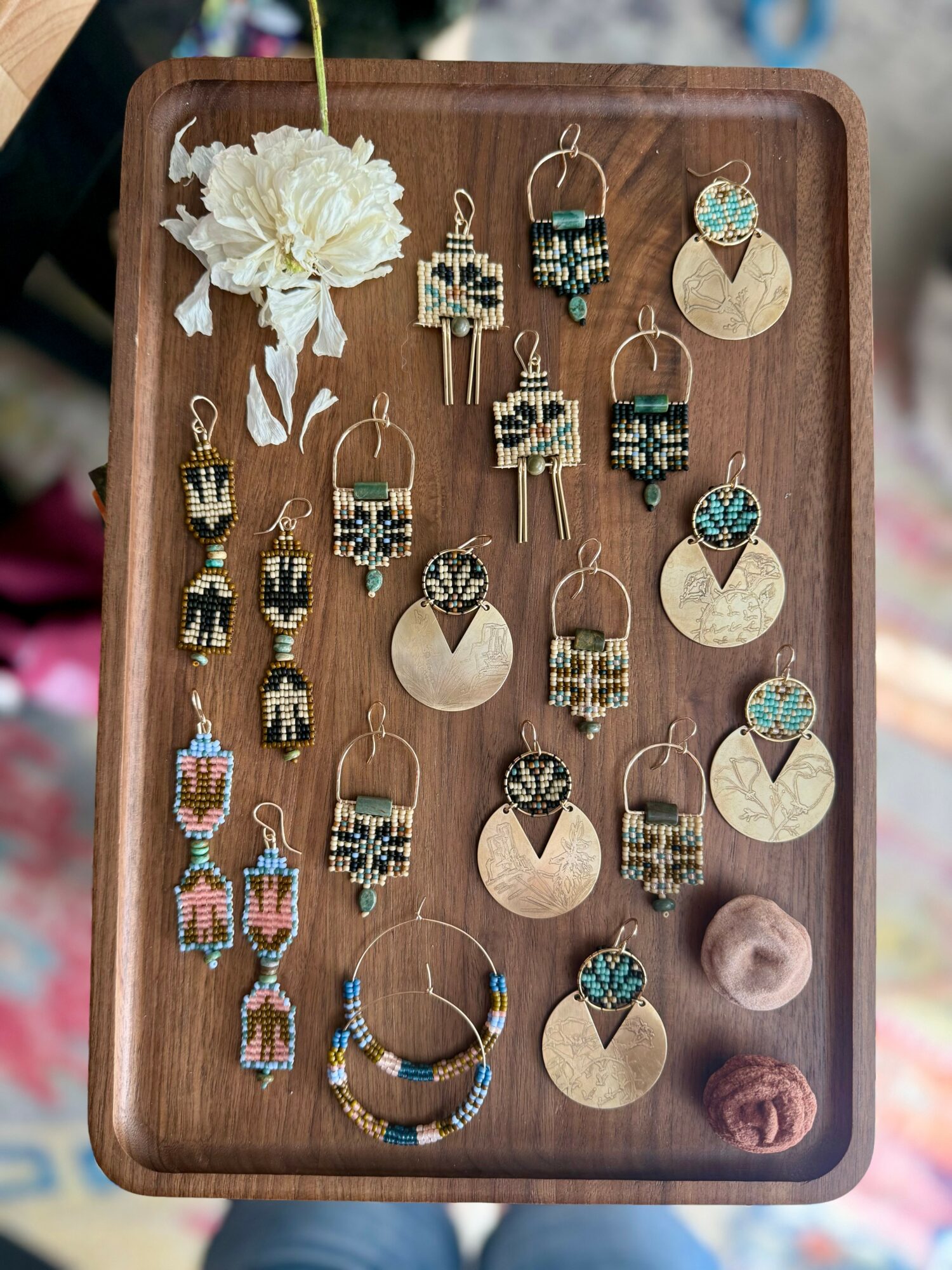 Display tray with colorful beaded earrings and necklaces, a flower, and decorative balls, arranged on a wooden surface.