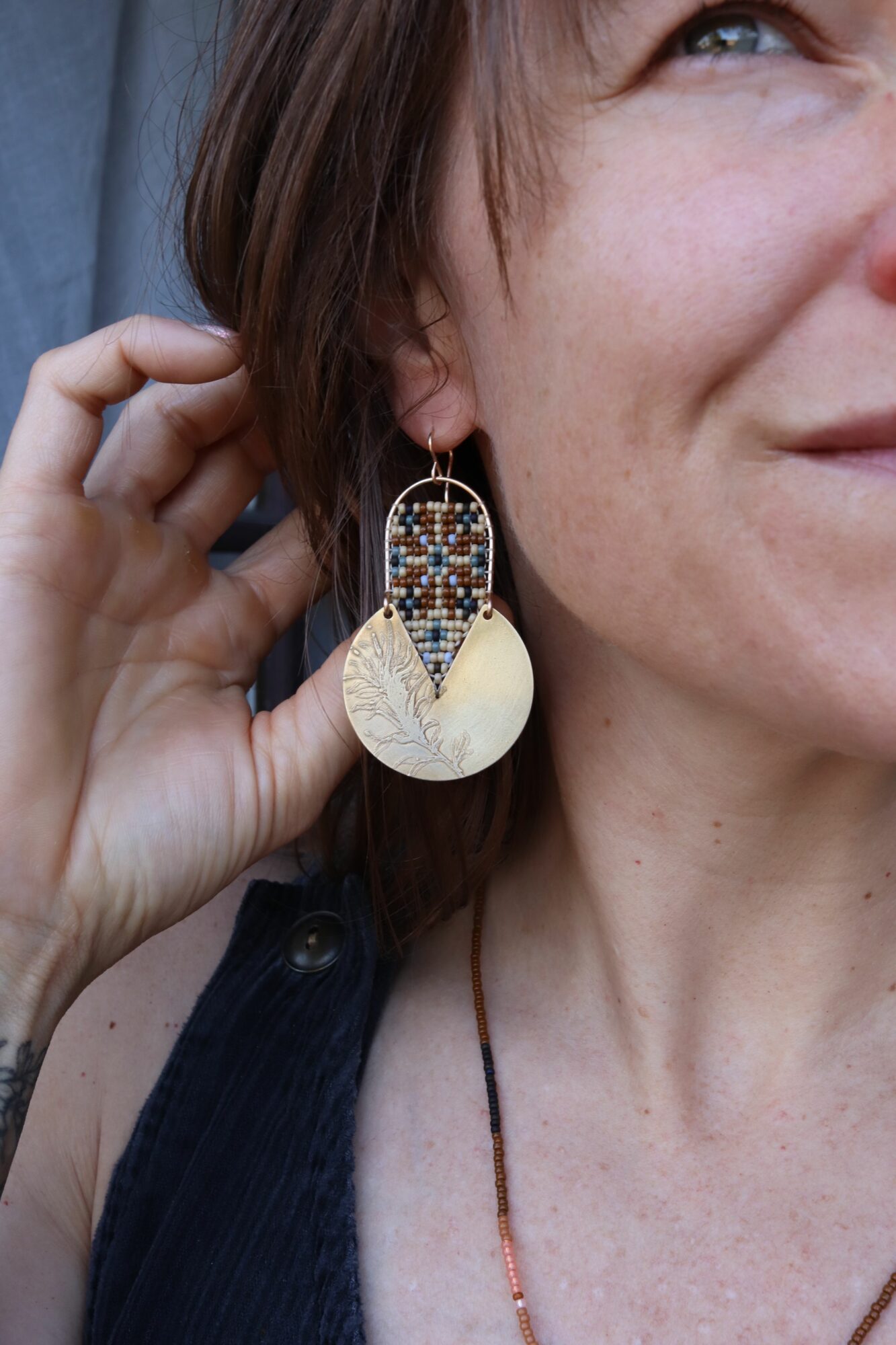Person with long hair holding an earring near their ear, showing part of their face and neck, wearing a dark top.