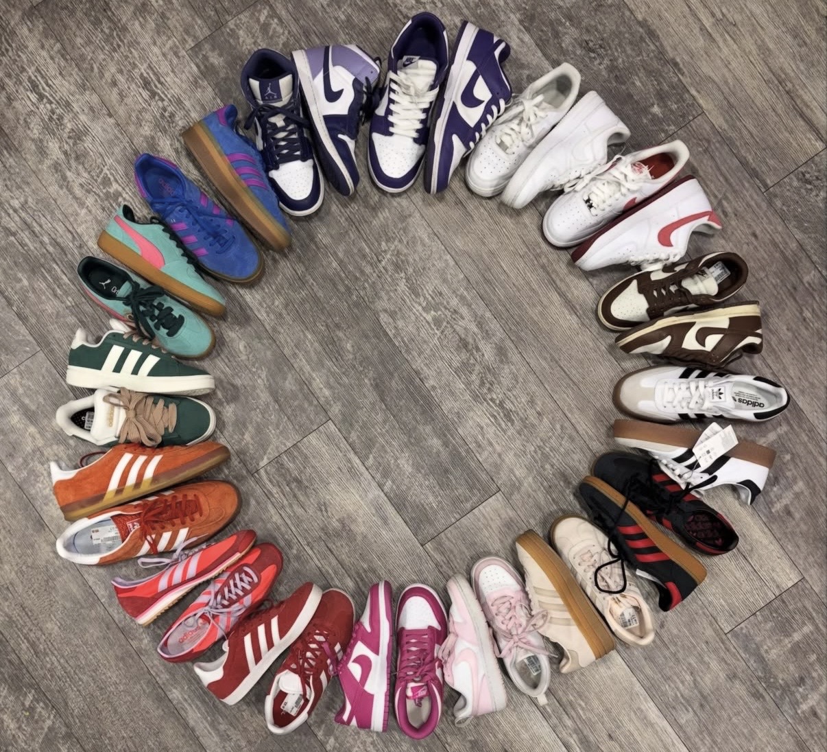 Collection of various sneakers arranged in a circle on a wooden floor, showing different colors and styles.