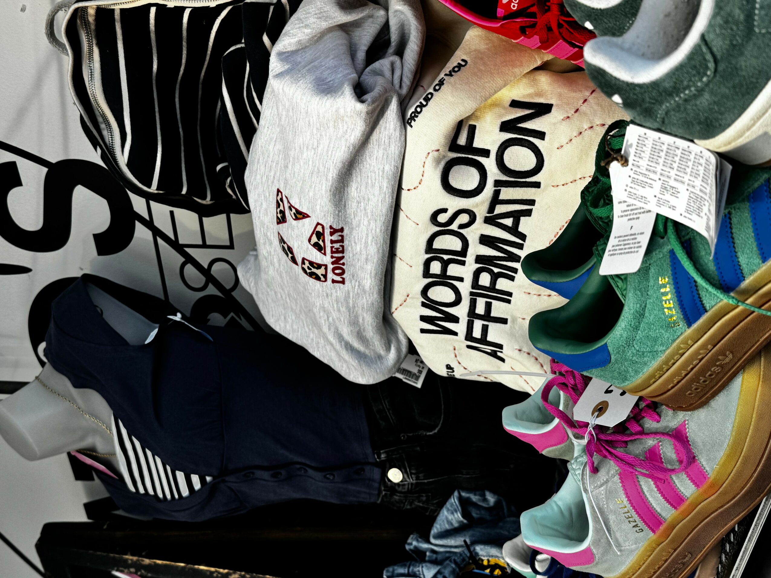 Clothes and bags on a surface, including a gray hoodie, a black and white striped bag, and colorful sneakers.