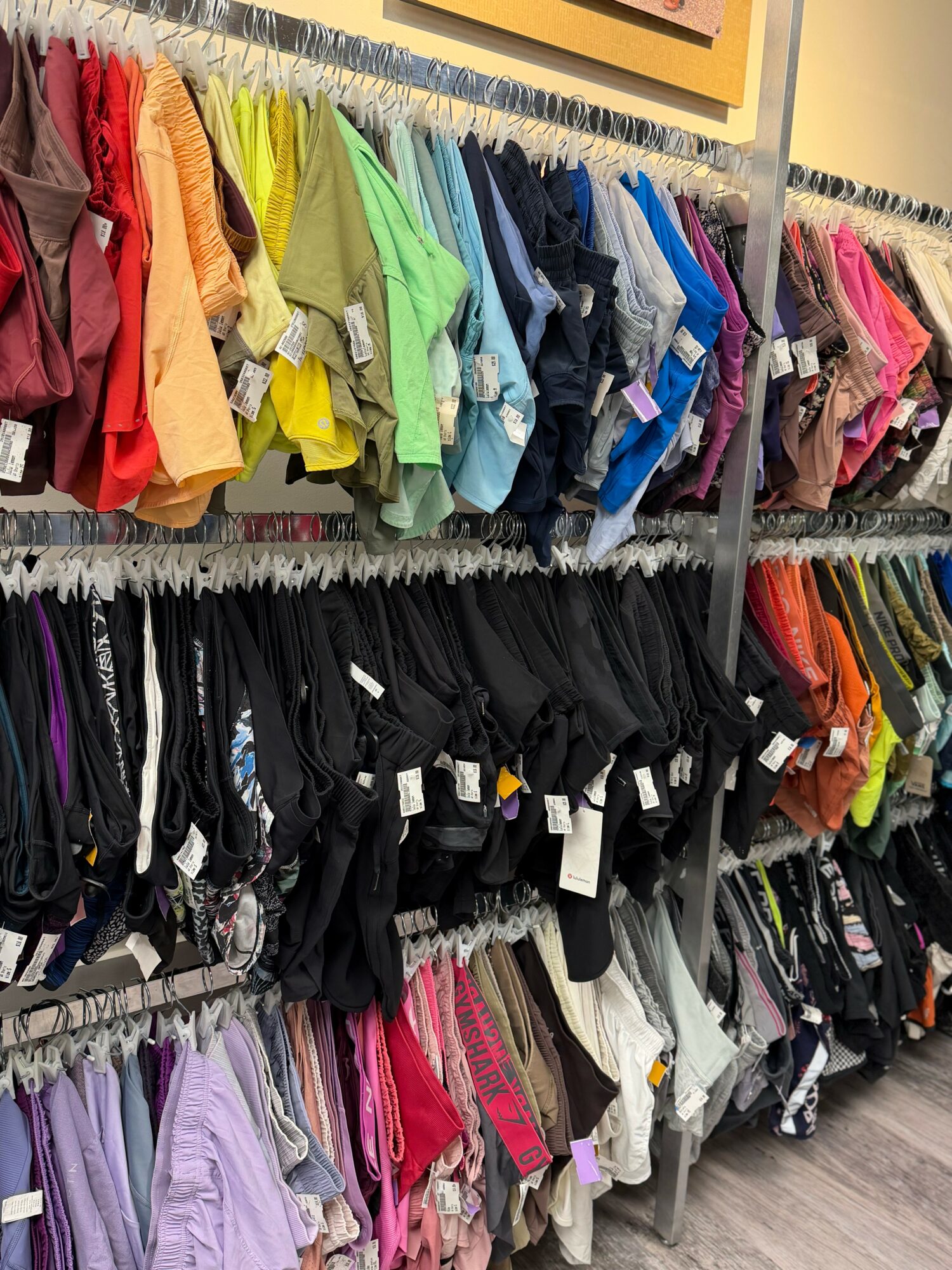 Clothing racks with colorful shirts, pants, and accessories in a store, organized by color and type.