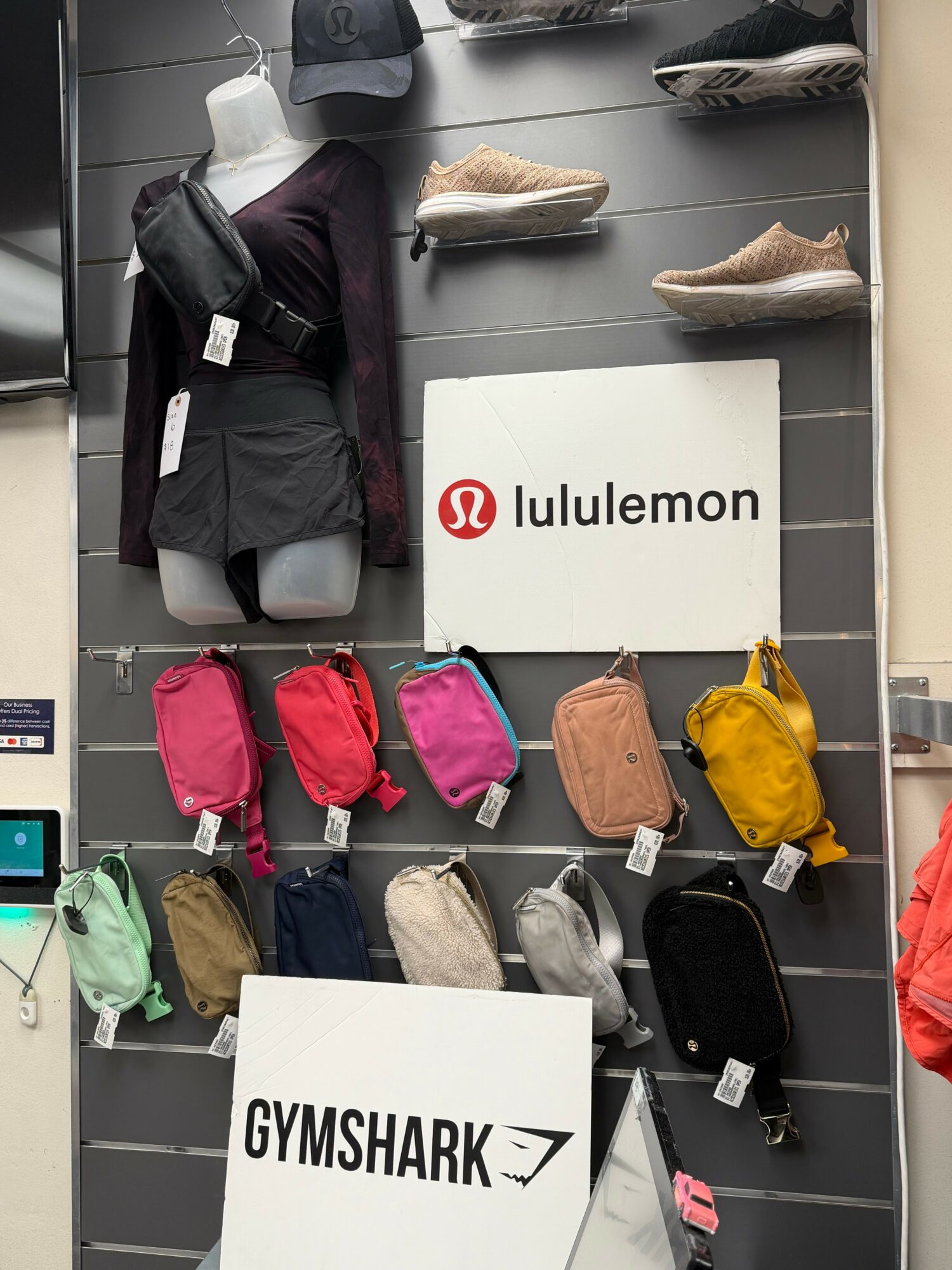 Display of backpacks, shoes, and hats with Lululemon and Gymshark signs on a wall.