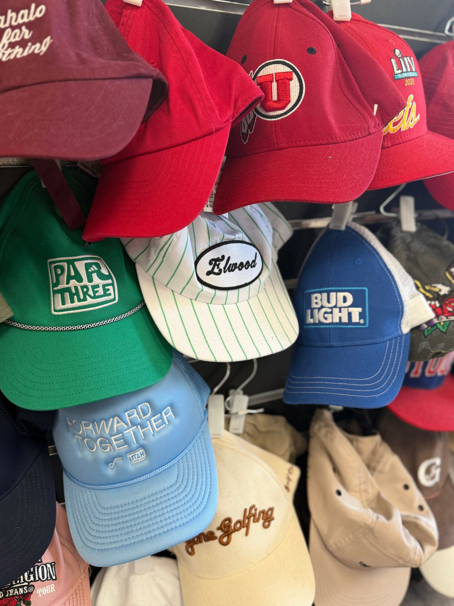 Collection of colorful baseball caps on display, including red, green, white, blue, and beige, with various logos and text.