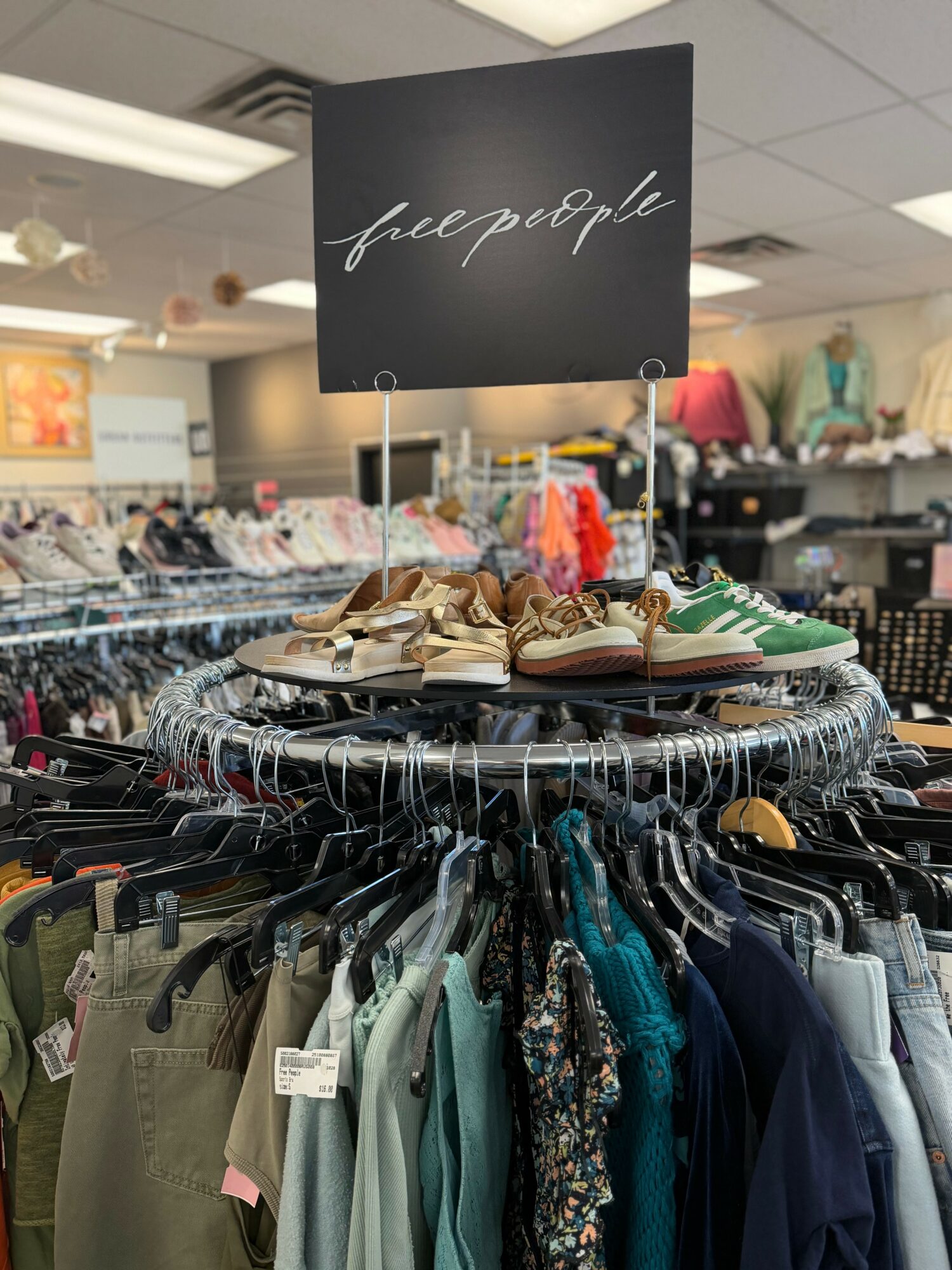 Clothing rack with shoes on top and various clothes hanging below, in a store setting, with a sign reading 'free people'.