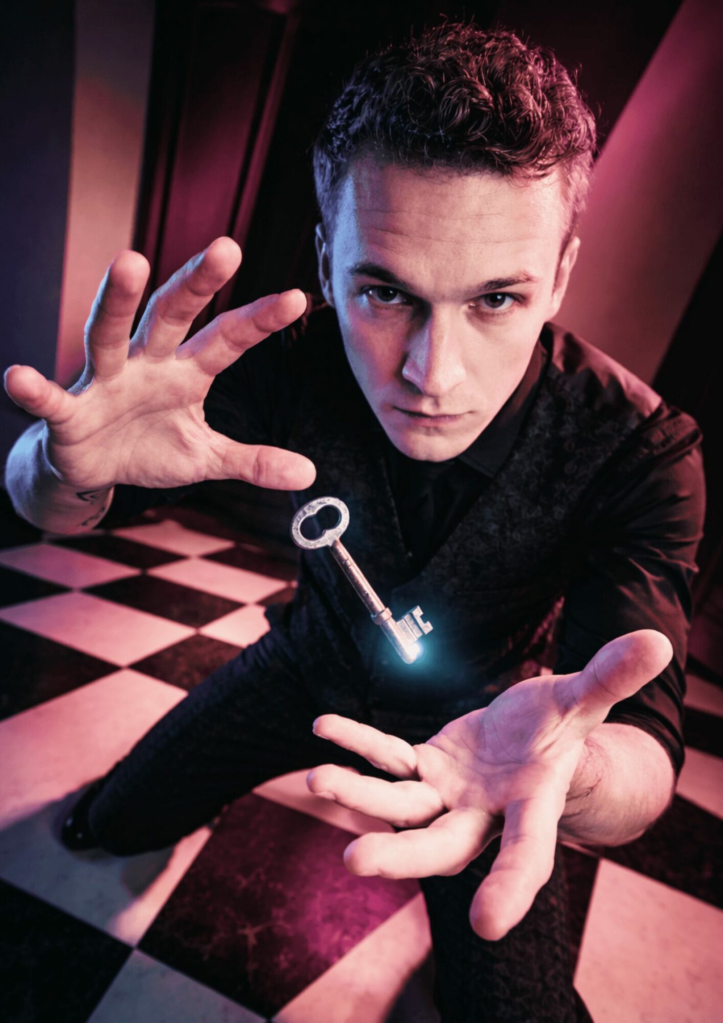 Young man with short hair reaching forward with a key glowing in his hand, in a checkered room, looking at the camera.