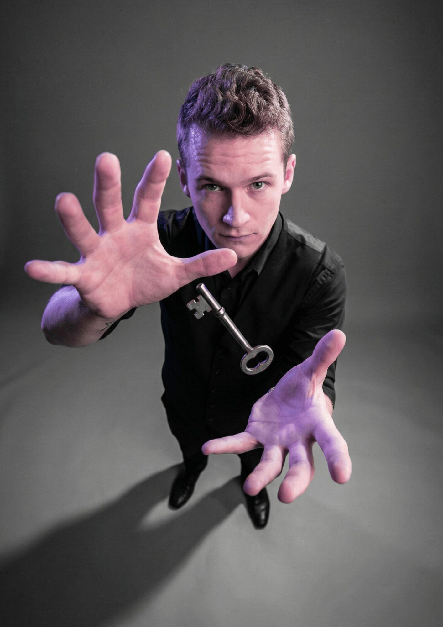 Young man reaching forward with both hands, holding a key, against a gray background.