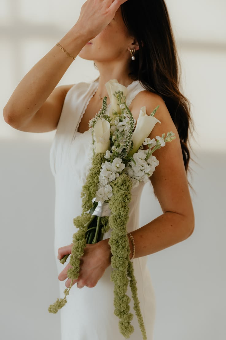 Woman holding a bouquet of white flowers, wearing a white dress, with her hand covering her face.