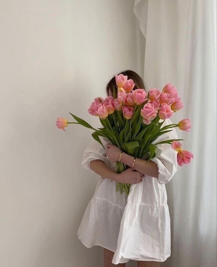 Child holding a large bouquet of pink tulips in front of a white wall and curtain.