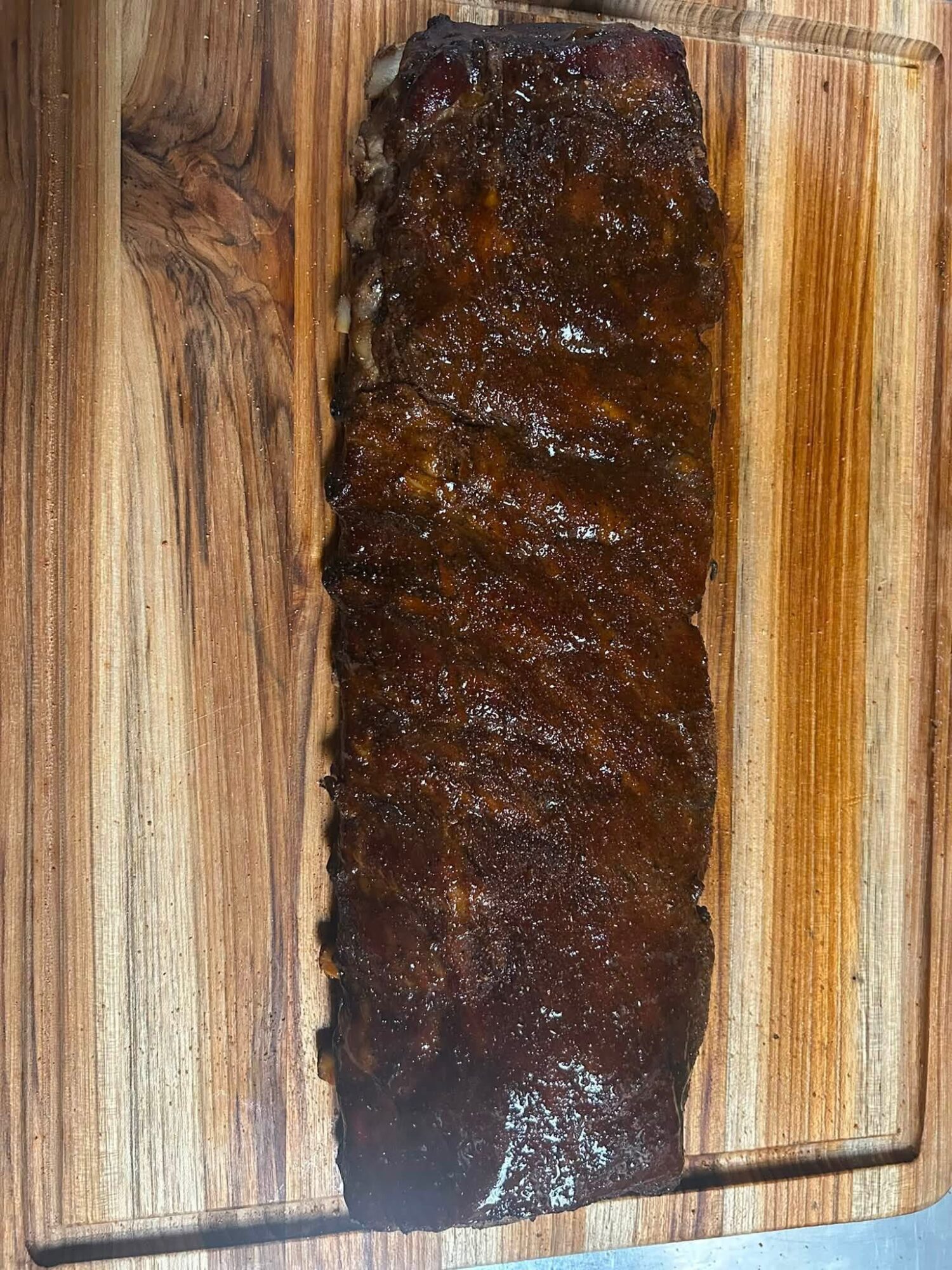 Barbecue ribs on a wooden cutting board, glazed with sauce, with a shiny surface and dark color.