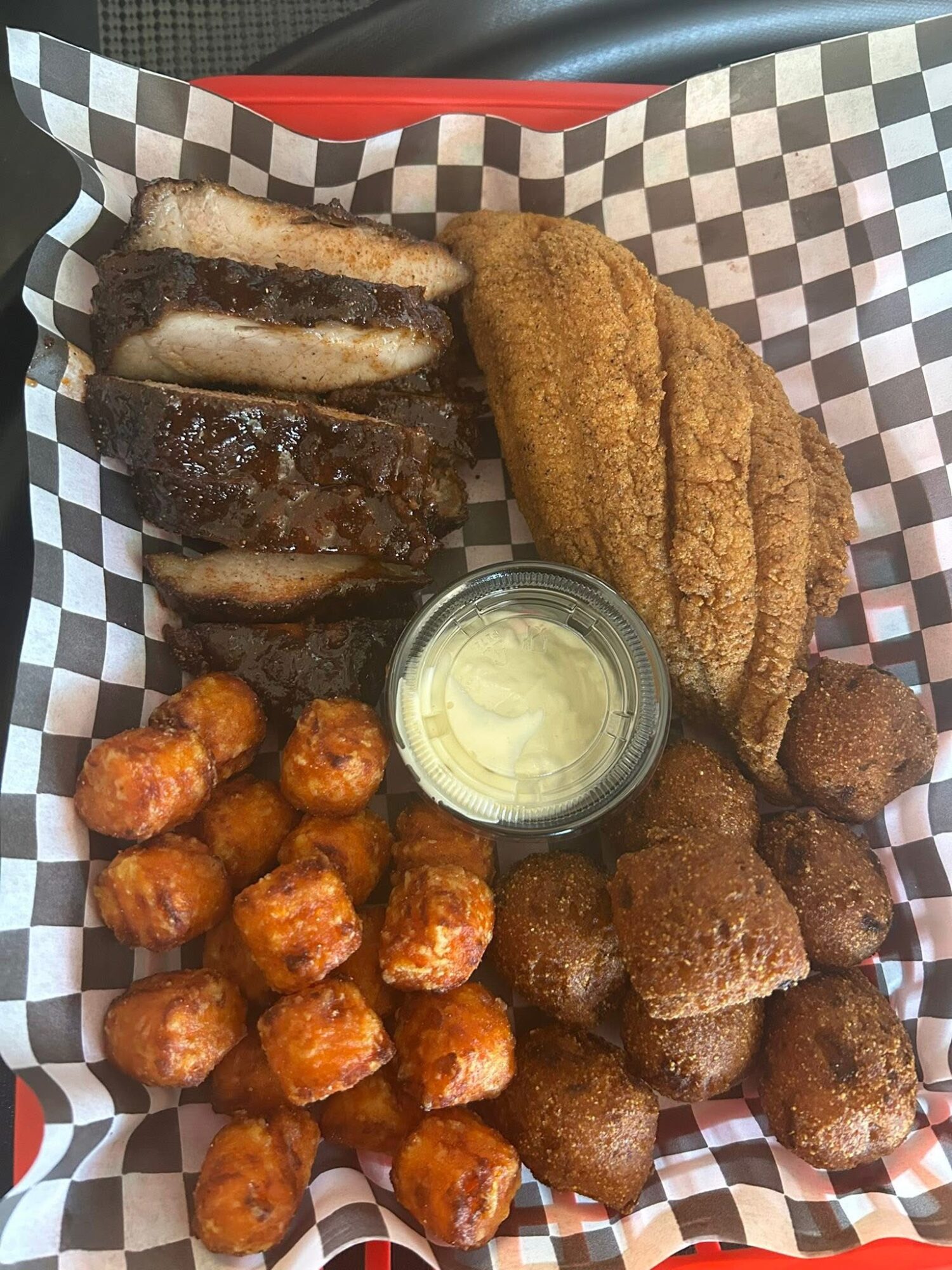 Assorted fried foods including chicken tenders, mozzarella sticks, and meatballs with dipping sauce on checkered paper.