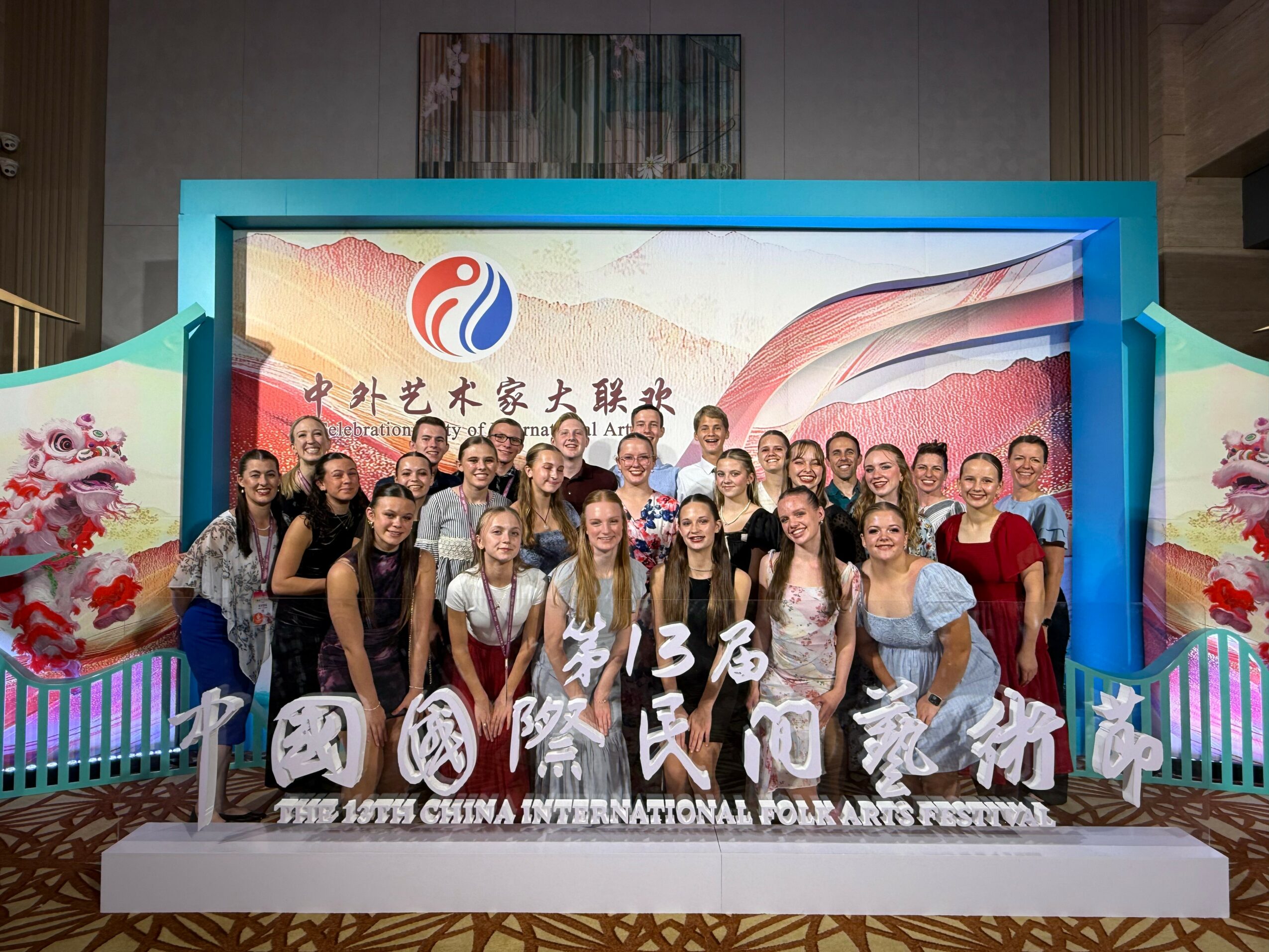 Group of people posing on stage at the 13th China International Folk Arts Festival, with colorful backdrop and decorations.