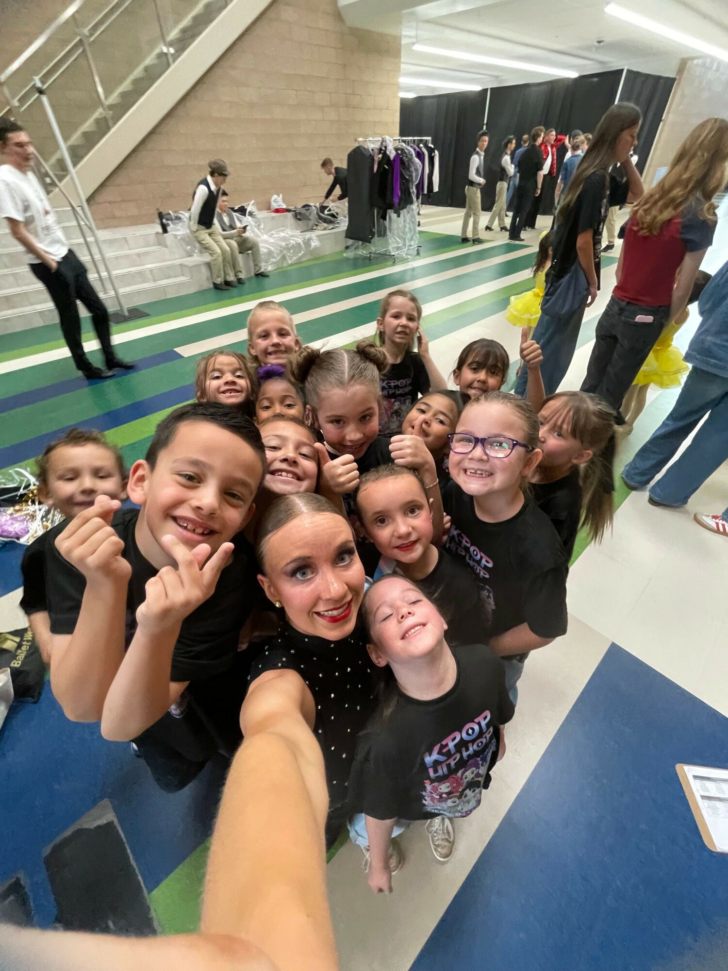Group of young women taking a selfie together indoors, some making peace signs, smiling, and posing for the camera.