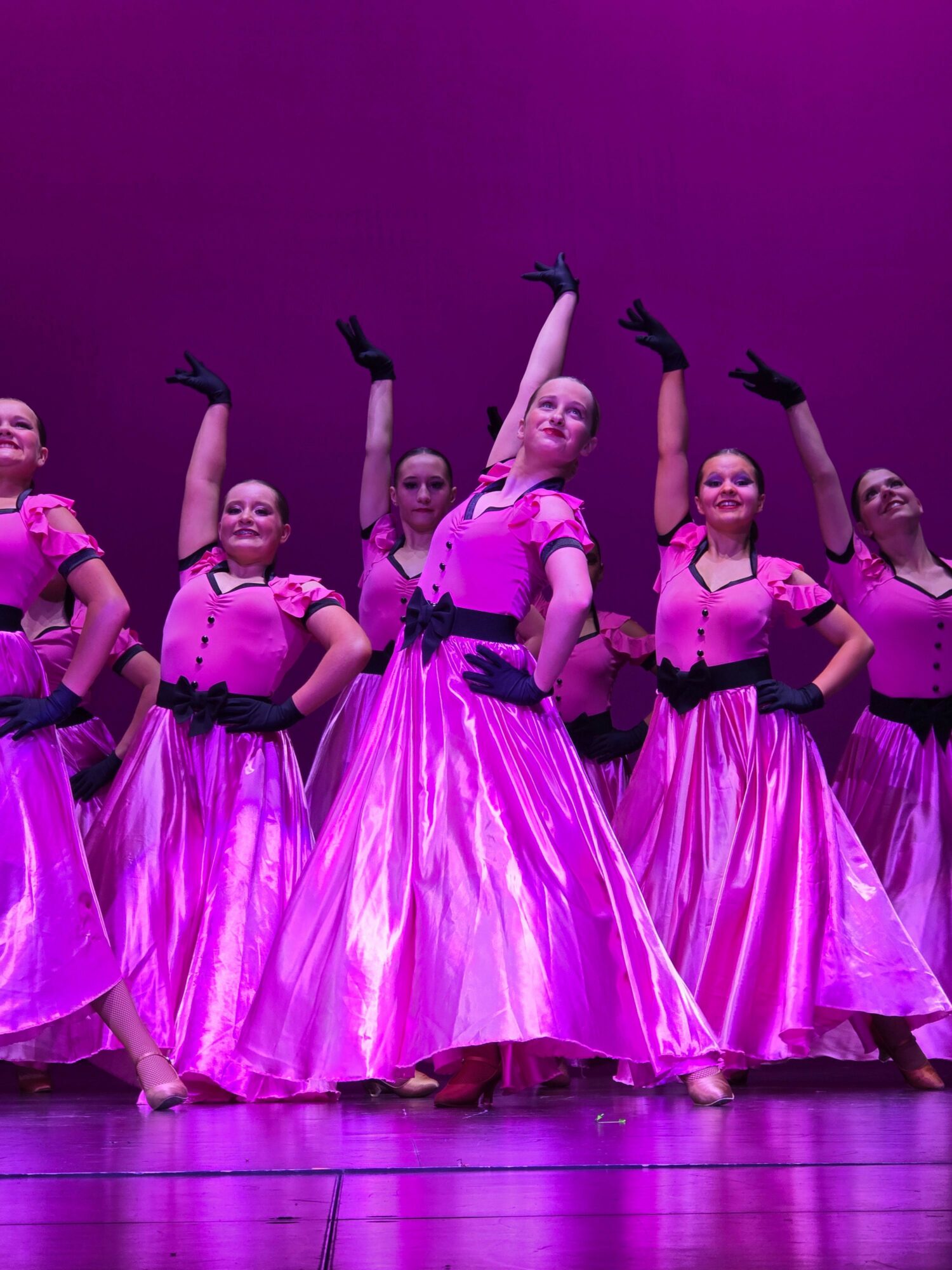 Group of five ballet dancers in pink costumes pose on stage with purple lighting.