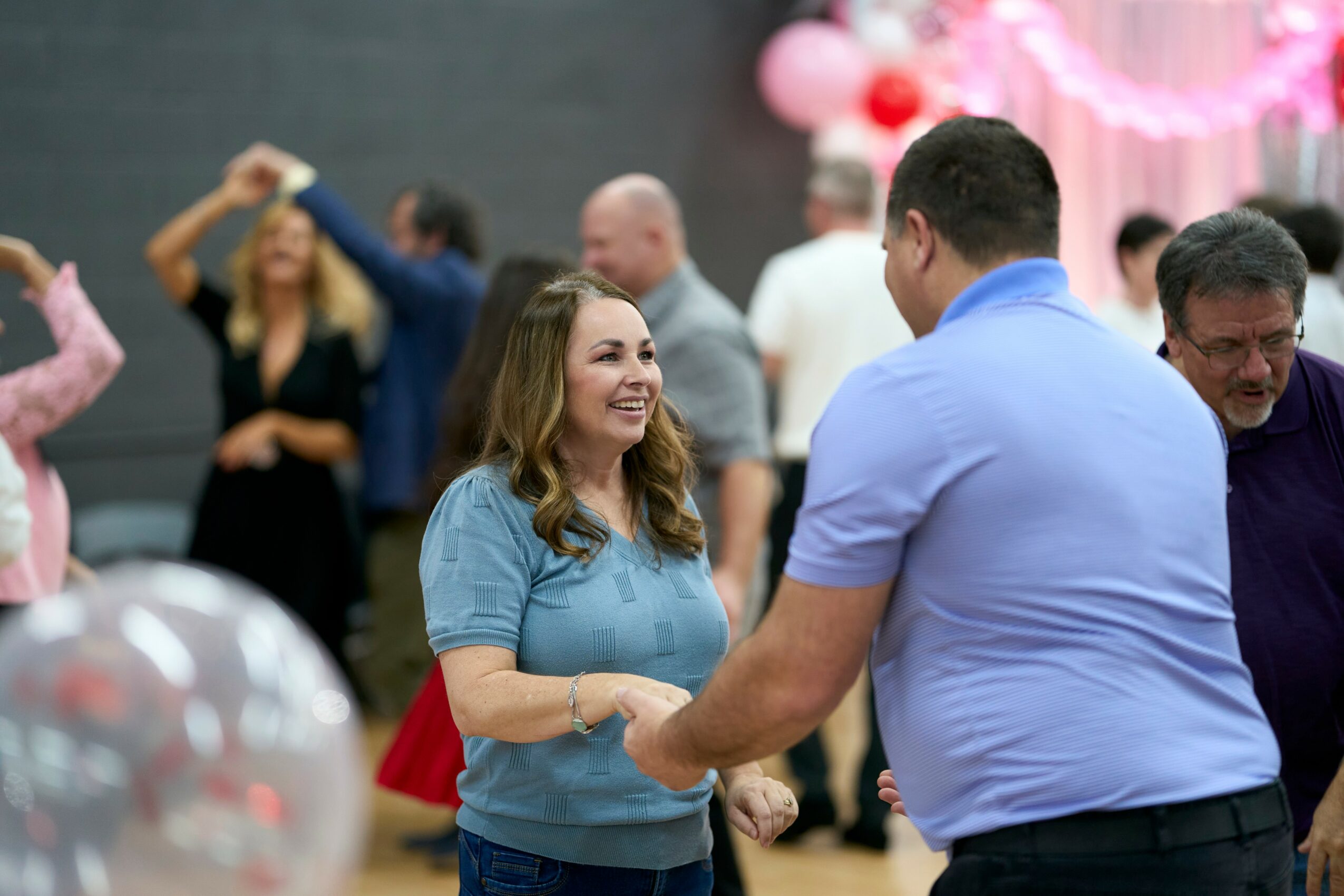People dancing and socializing at a celebration with pink decorations in the background.