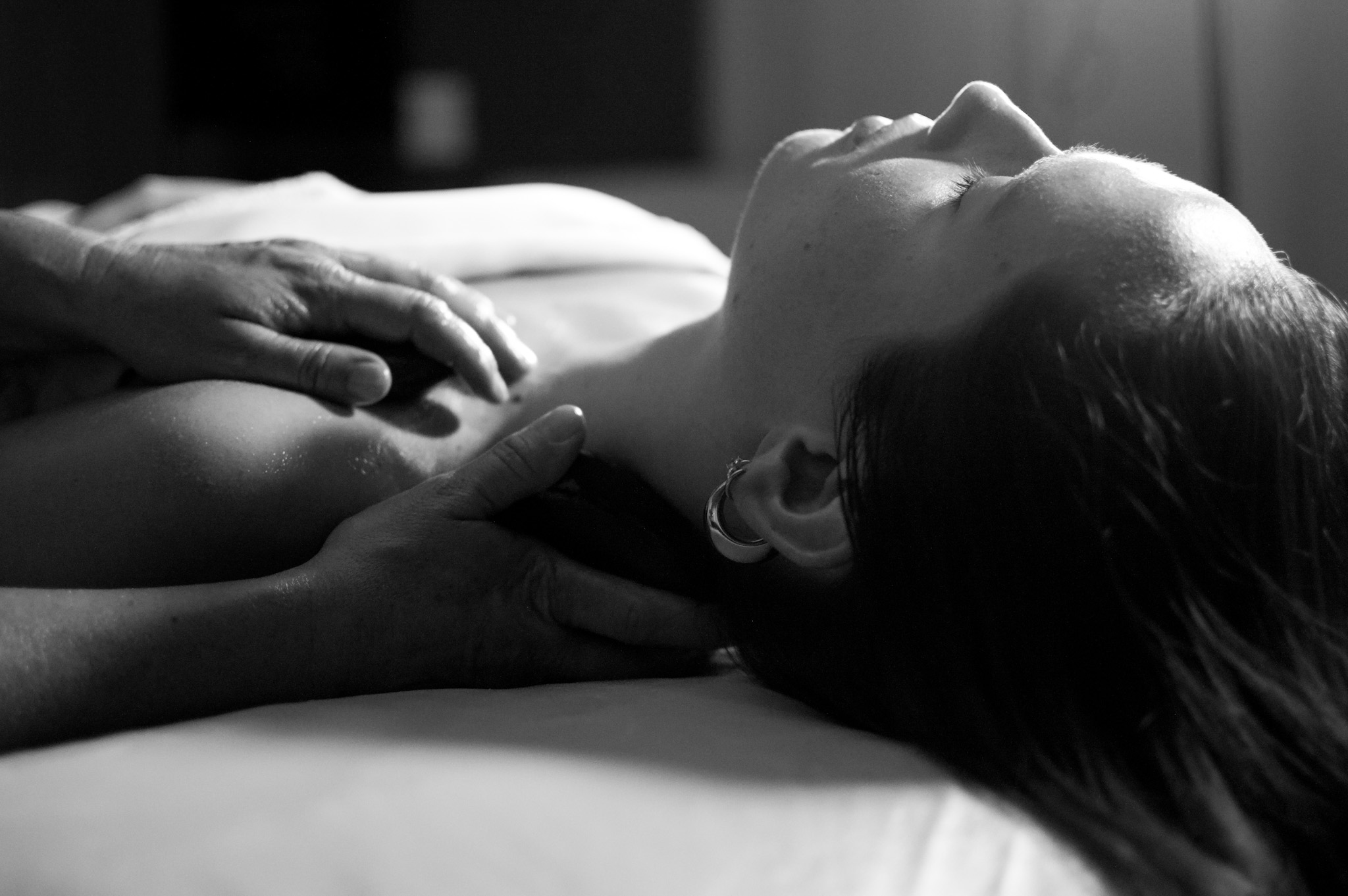 Person lying on bed with hands gently touching their neck, in black and white.