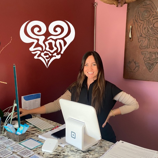 Woman smiling at desk with computer, in a room with pink and maroon walls, and artwork on the wall.