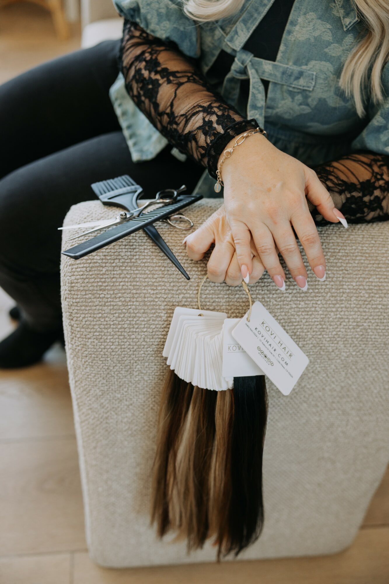 Person with lace sleeves resting hand on beige fabric-covered display with hair color sample and tags, in a retail setting.