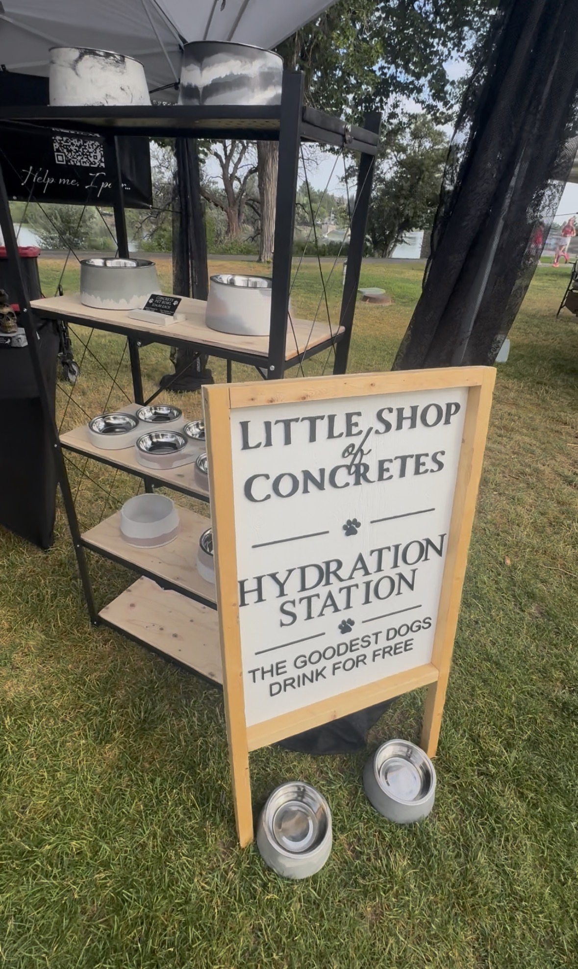 A sign for a hydration station with two metal bowls on grass, and a shelf with supplies behind it.