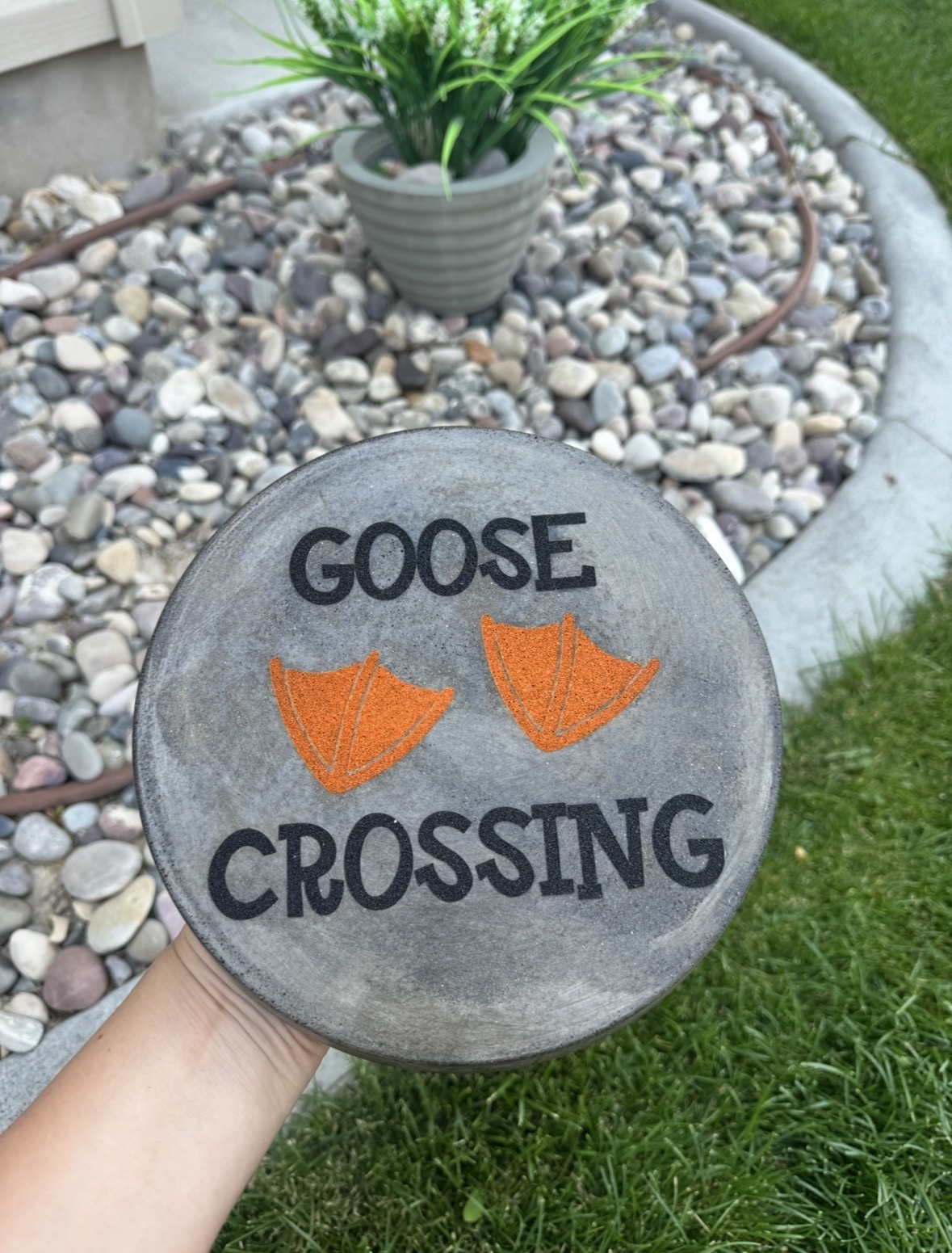 Hand holding a round sign with orange goose footprints and the words 