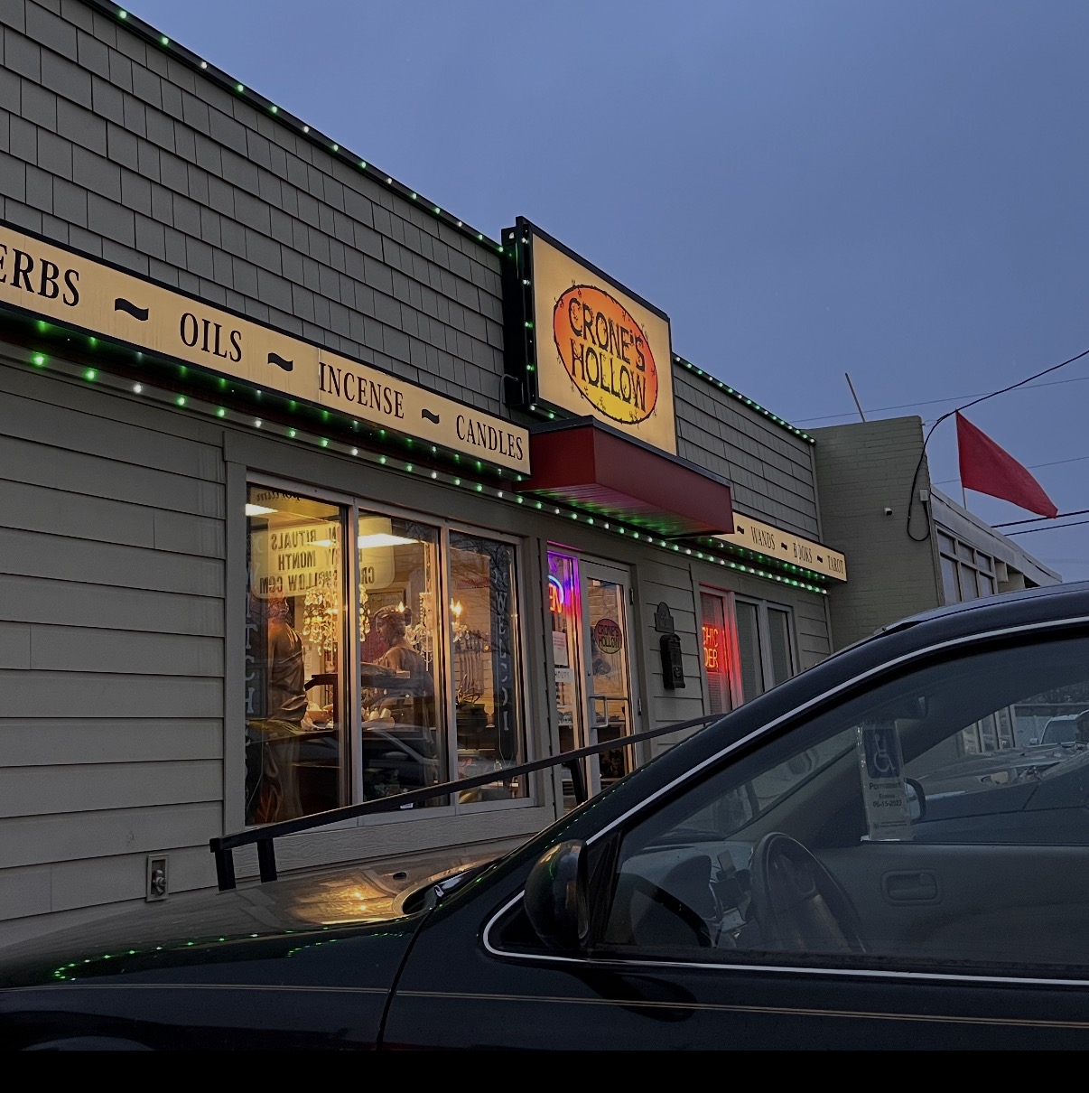 Storefront with a sign reading 'CROAK & HOLLOW' and a window display, with a car in front, under a blue sky.