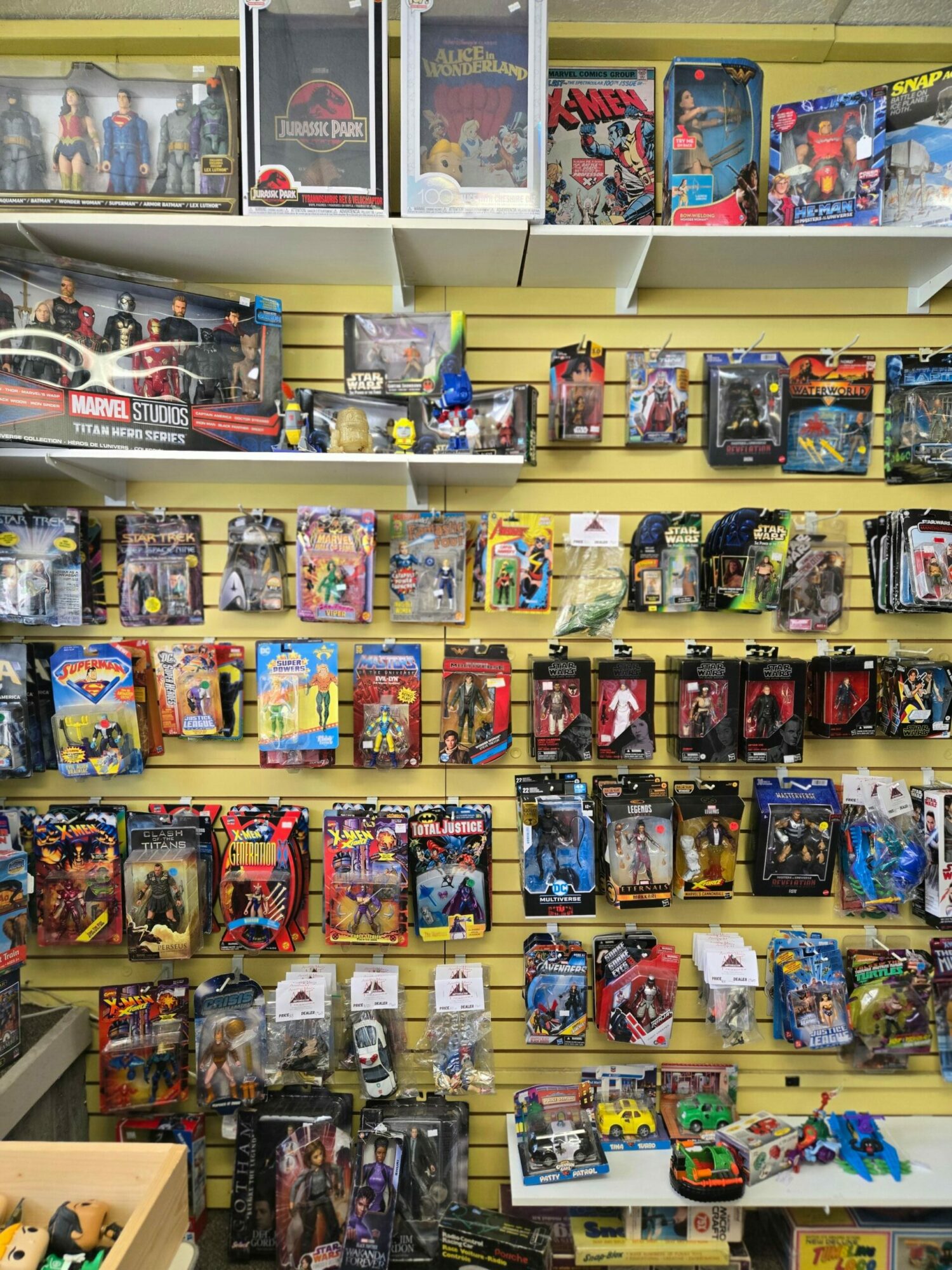 Shelves filled with colorful action figures and toys, organized in rows, with some packaging visible on the left side.