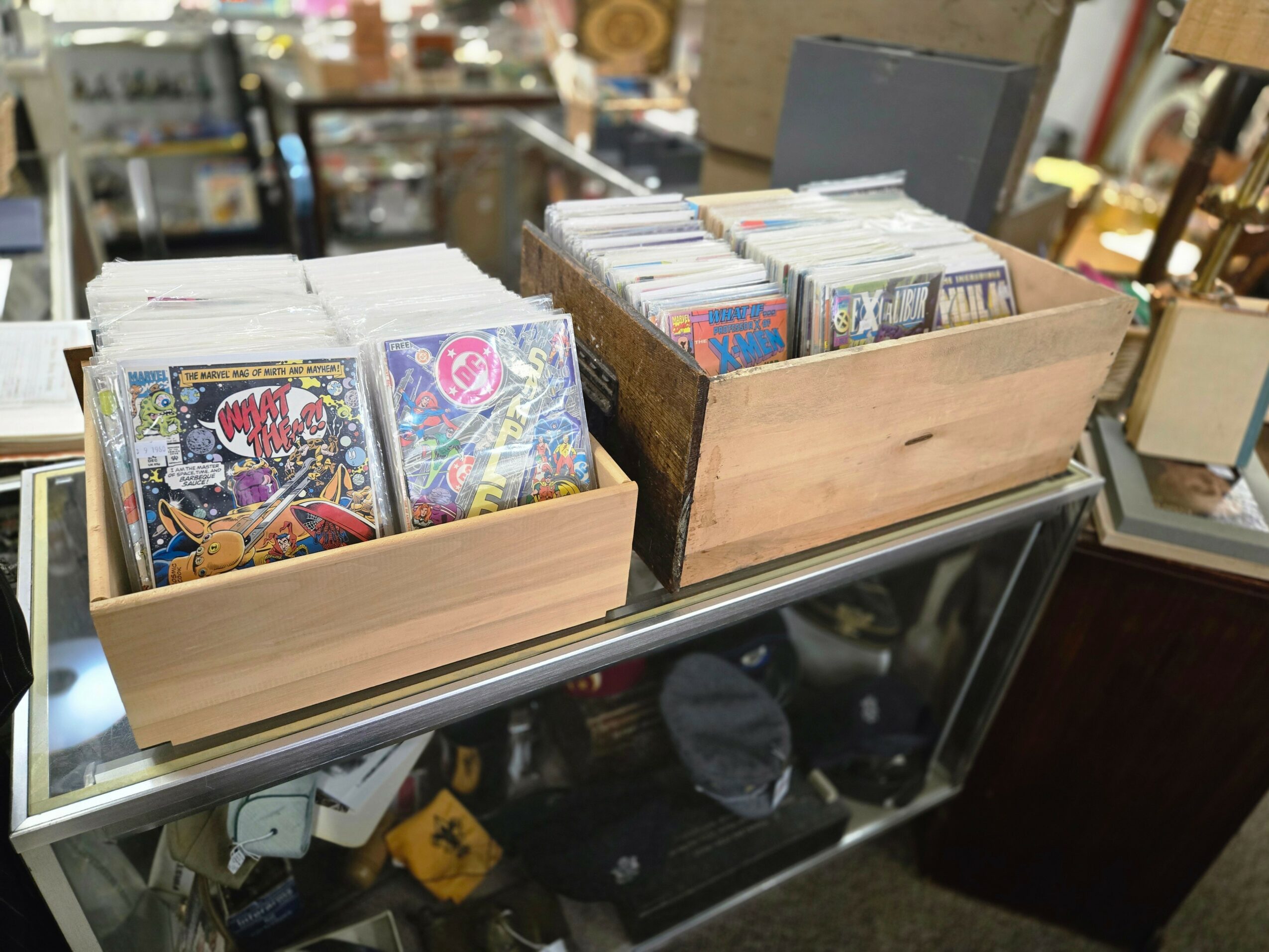 Two wooden boxes filled with comic books on a glass display case in a store, with various items in the background.