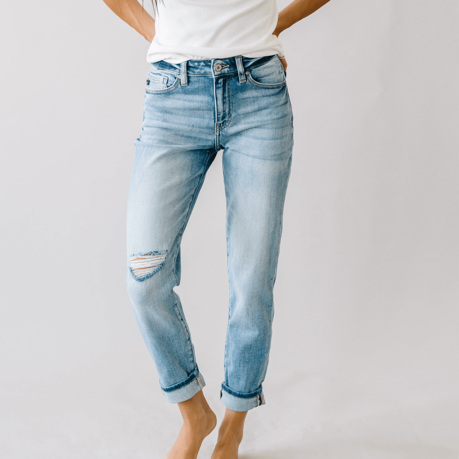 Person wearing light blue ripped jeans and a white top, standing barefoot against a plain background.