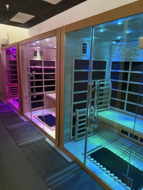 Two glass sauna rooms with colorful lighting, one pink and one blue, in a modern indoor setting.