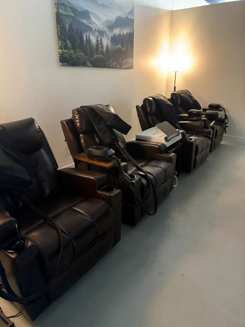 Row of black and brown bags and backpacks on a light-colored floor against a white wall with a landscape painting.