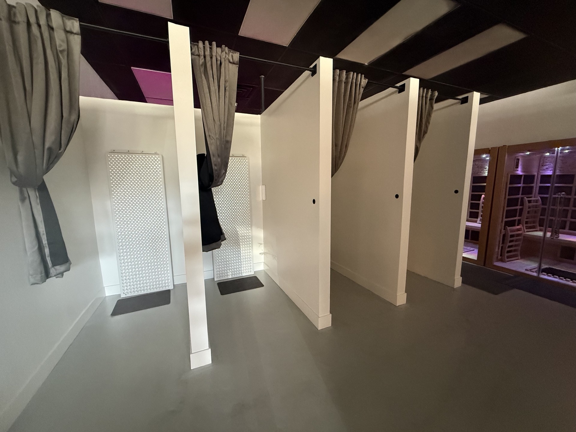 Three changing stalls with white partitions, gray curtains, and a gray floor, in a room with a window and balcony.