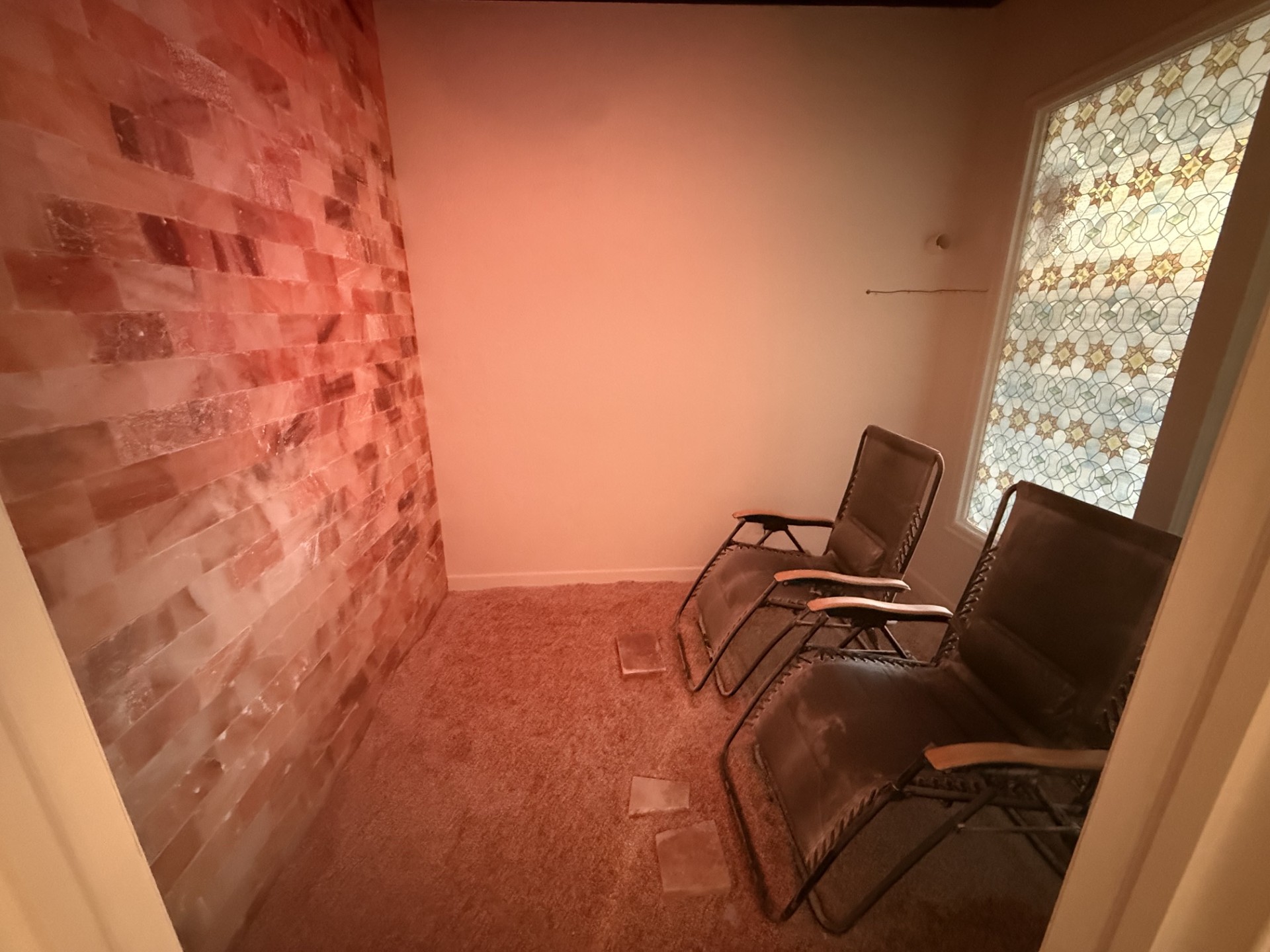 Small room with brick wall, two chairs, window with patterned curtain, carpeted floor, and plain wall.
