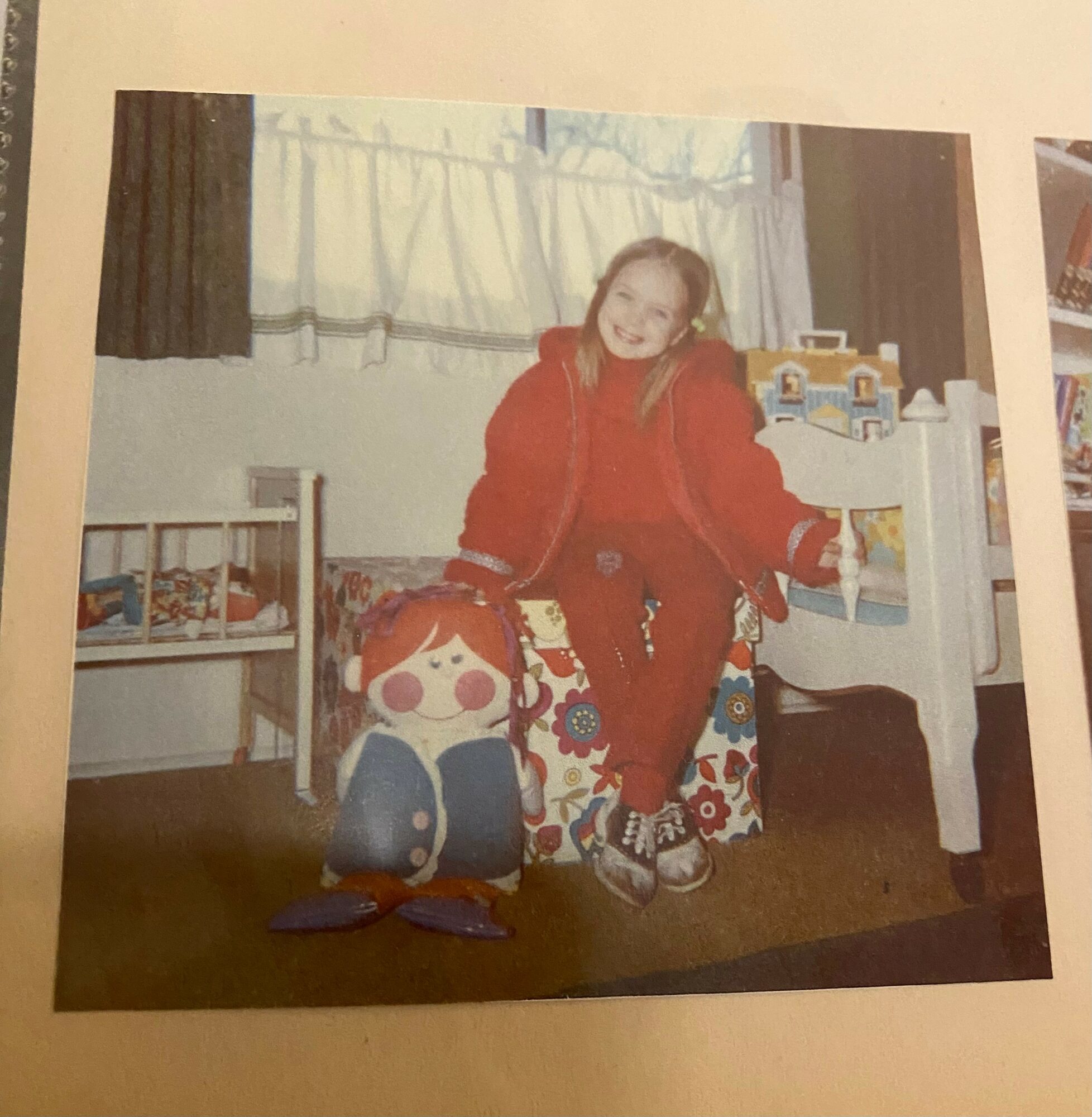 Child in red jacket standing next to a large cartoon character figure in a room with beds and curtains.