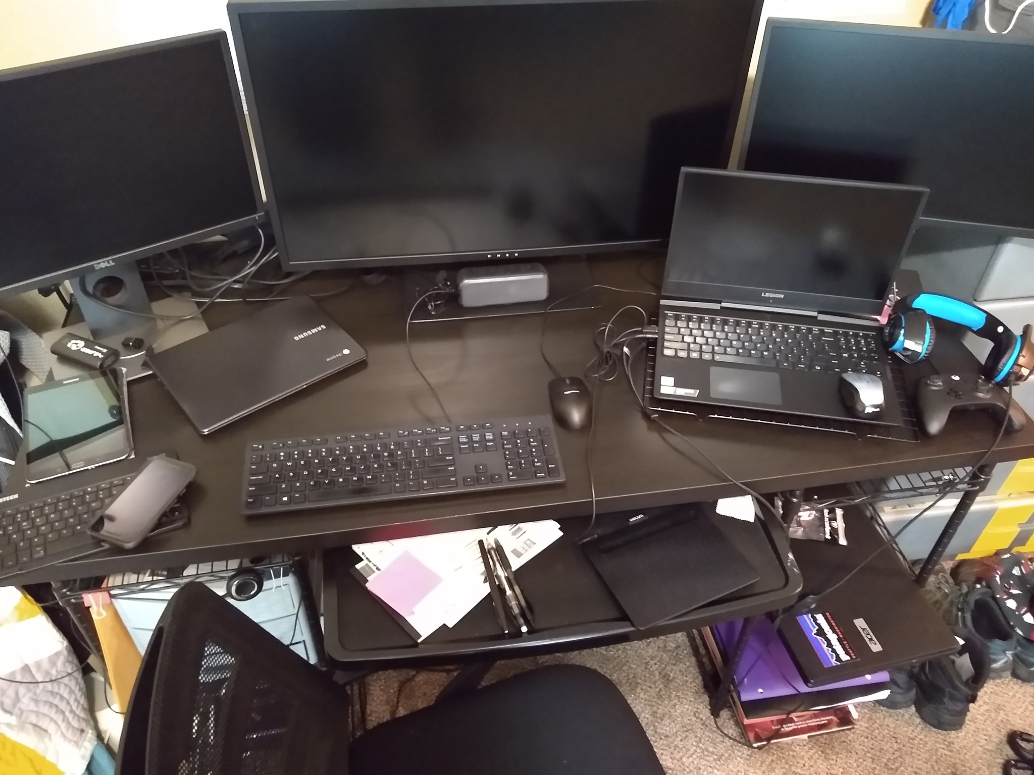 Multiple computer monitors, a laptop, keyboard, mouse, and headphones on a desk with papers and electronic devices.