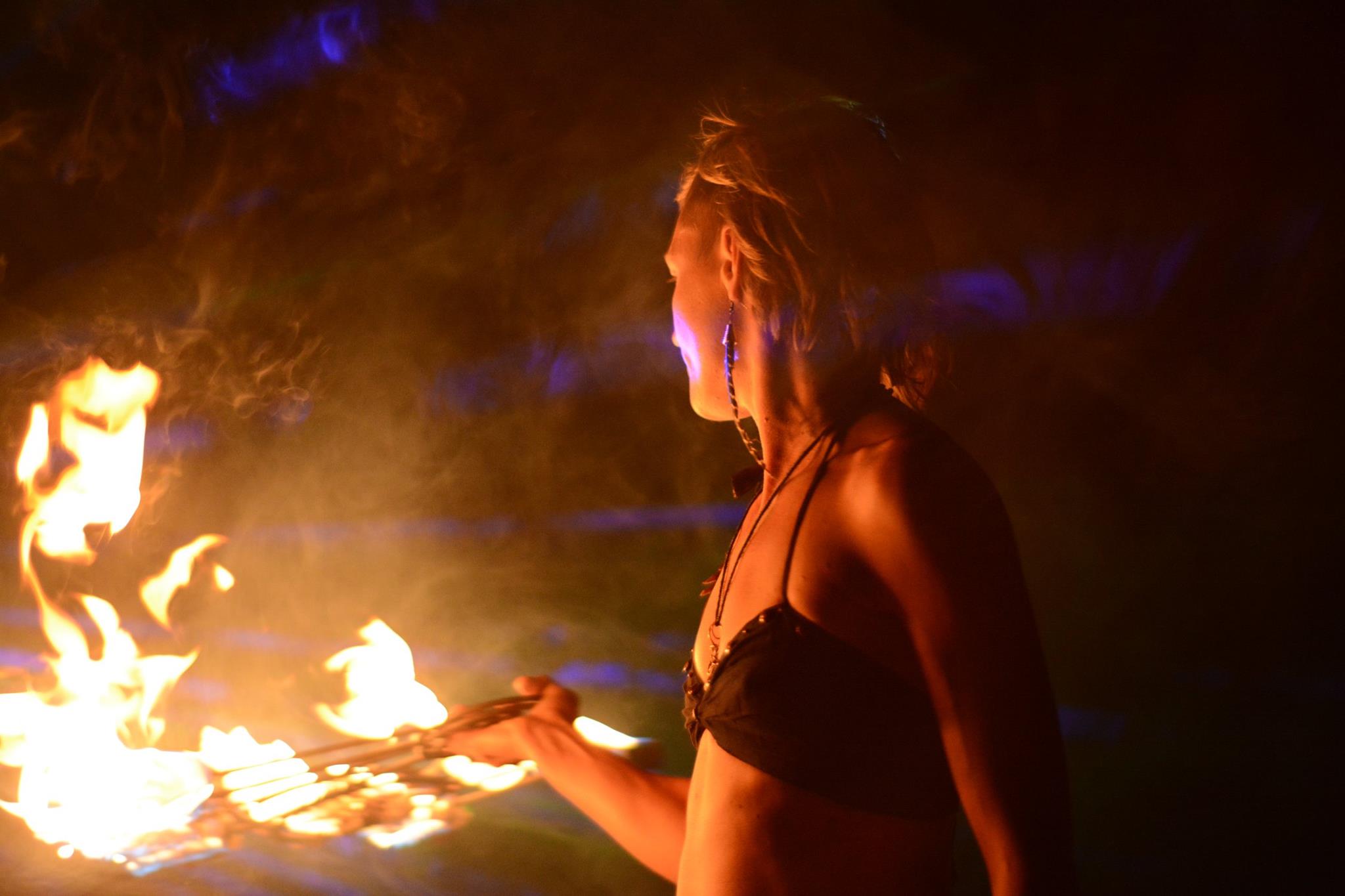 Person holding a flaming object in a dark environment, with visible fire and smoke, facing sideways.