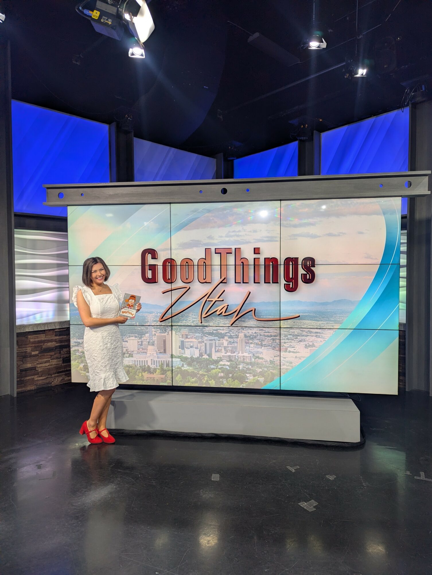 Woman standing in front of a large screen displaying 'Good Things' and 'Uptown' with a cityscape background.