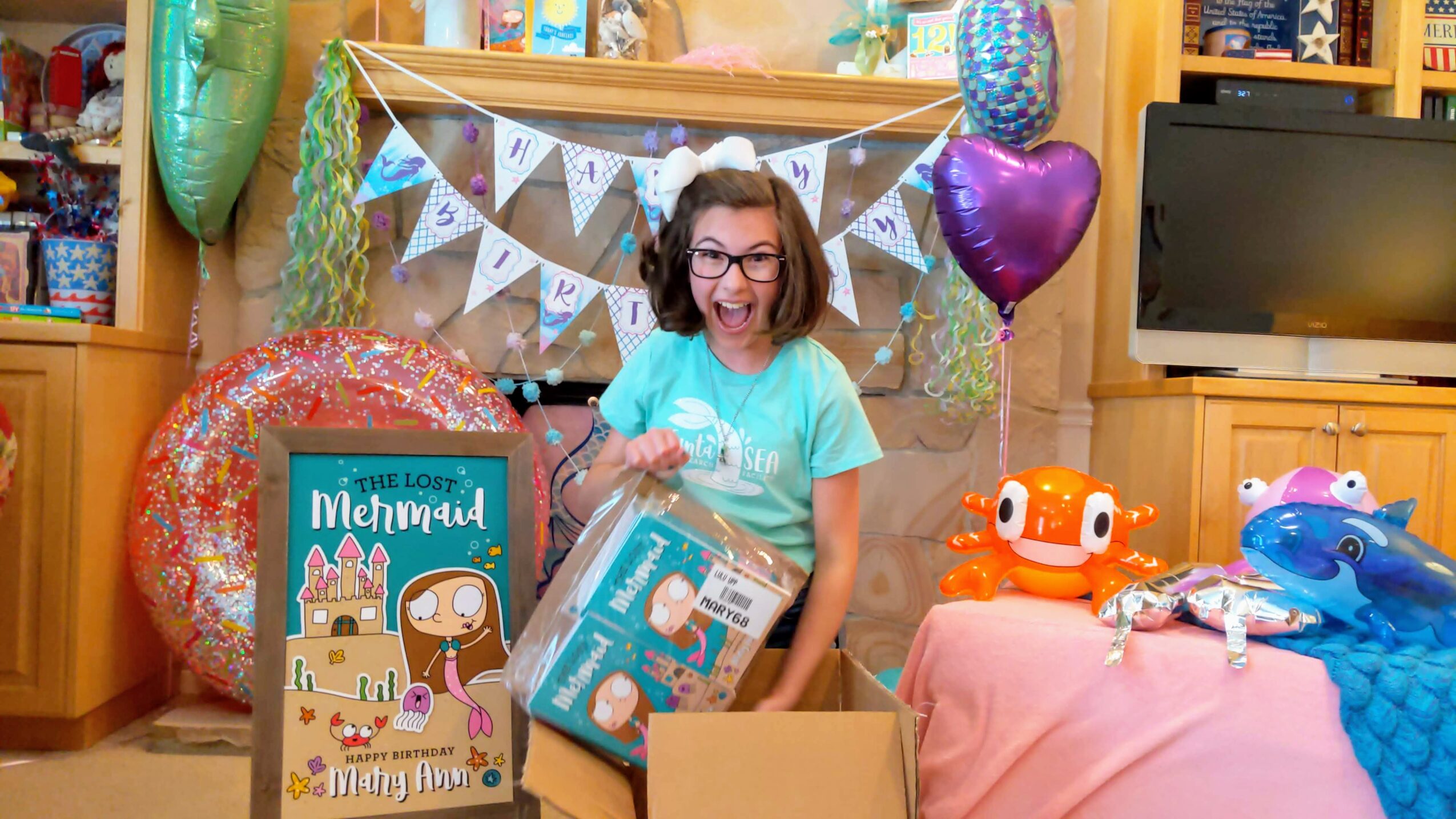 Child with glasses opening a gift at a birthday party with mermaid-themed decorations and toys on the table.
