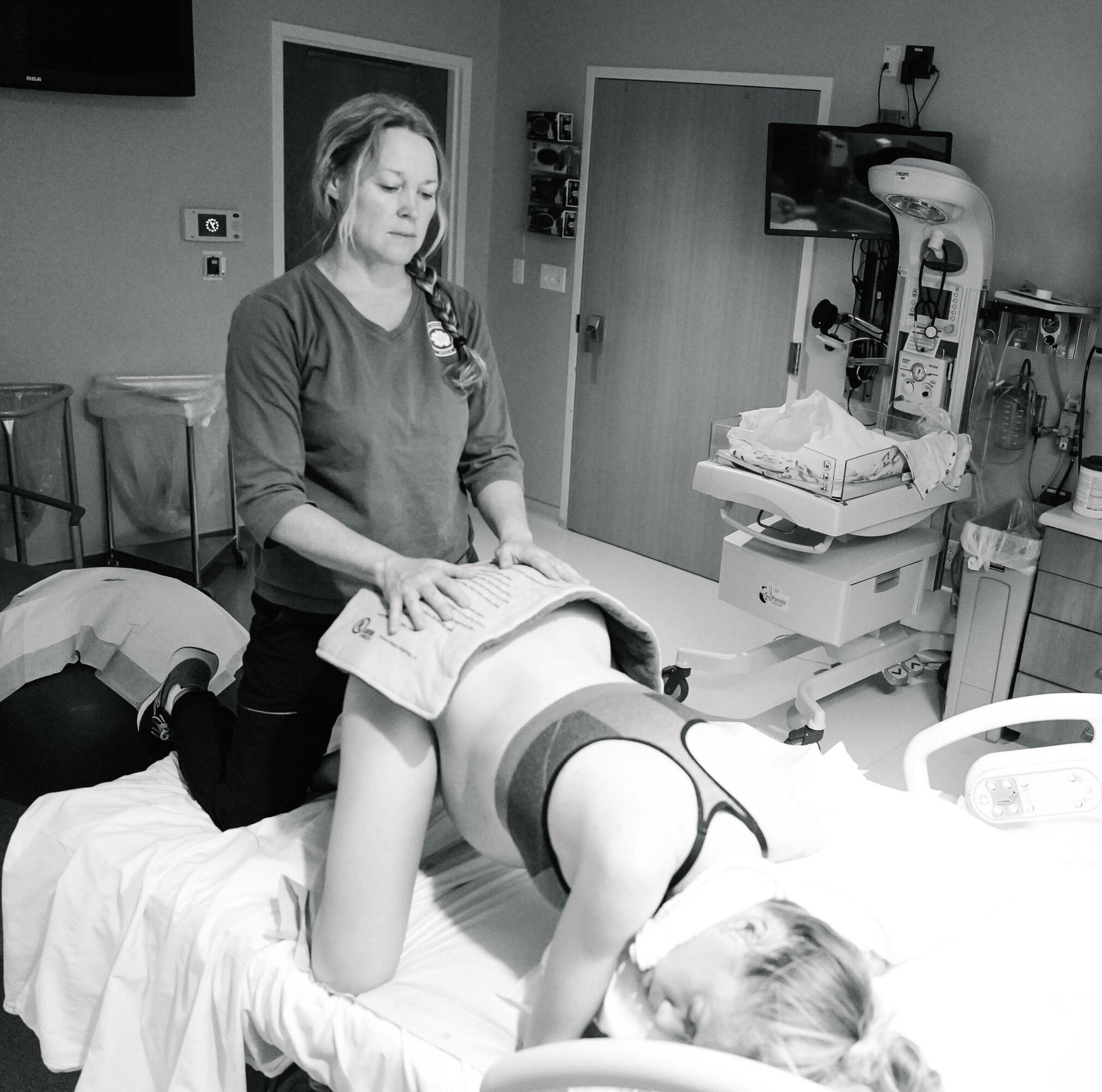 A woman appears to be preparing a medical procedure on a patient lying face down on a hospital bed, in a clinical setting.