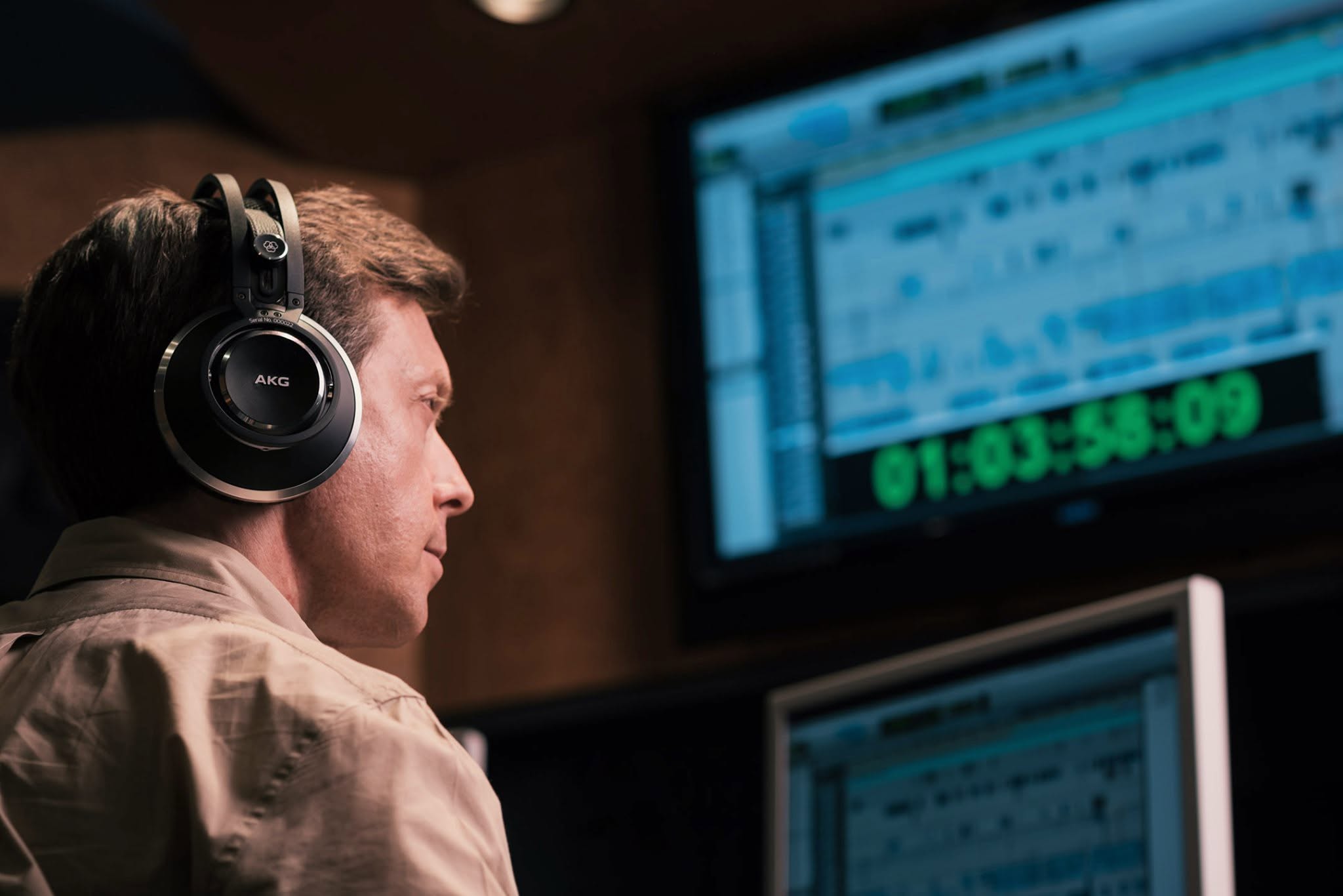 Young man wearing headphones working on music production software on a computer screen, in a studio setting.