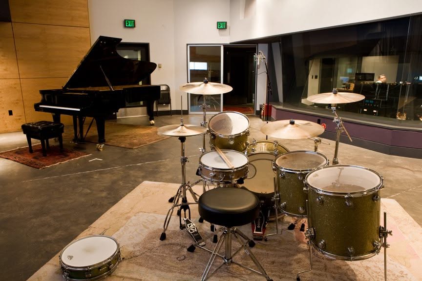 Music room with a drum set in the foreground and a grand piano in the background, with a mirror on the right wall.