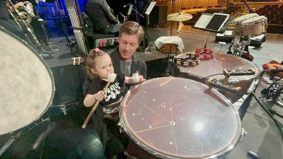 Adult and child playing drums in a music studio with various instruments and equipment around them.