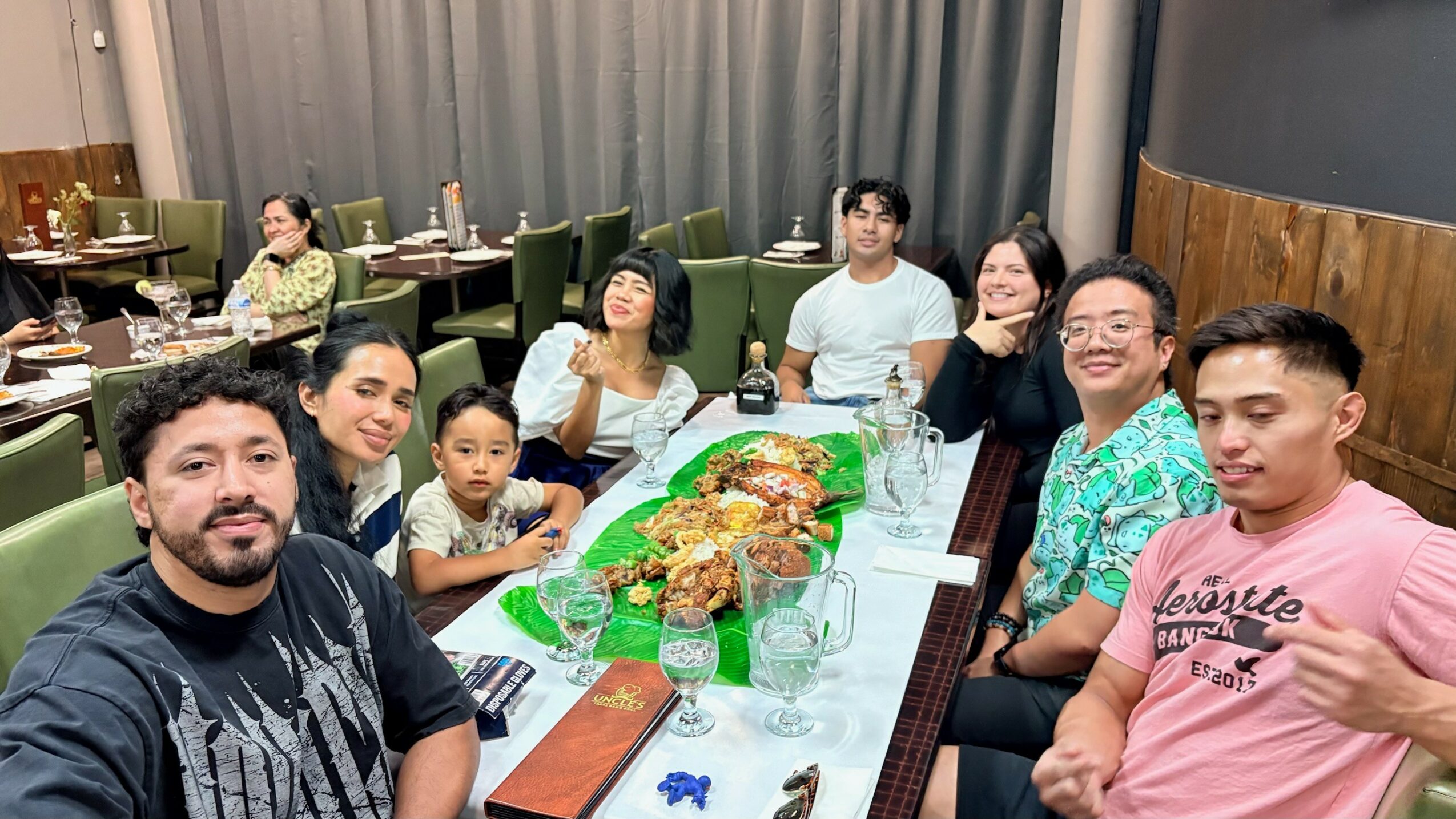Group of ten people sitting around a table in a restaurant, with food and drinks, smiling and posing for the photo.