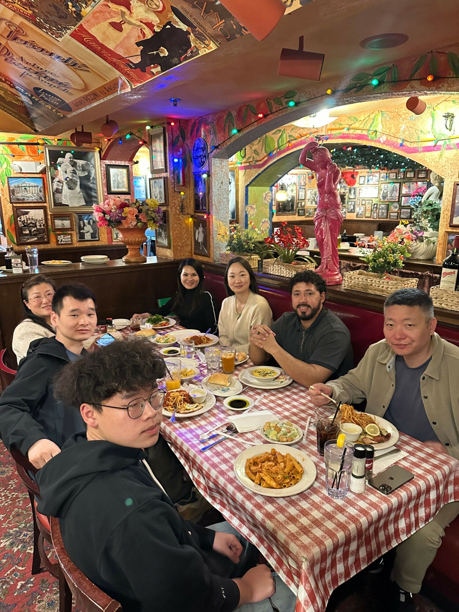 Group of people sitting at a table with food in a decorated restaurant, colorful lights and arcade games in background.