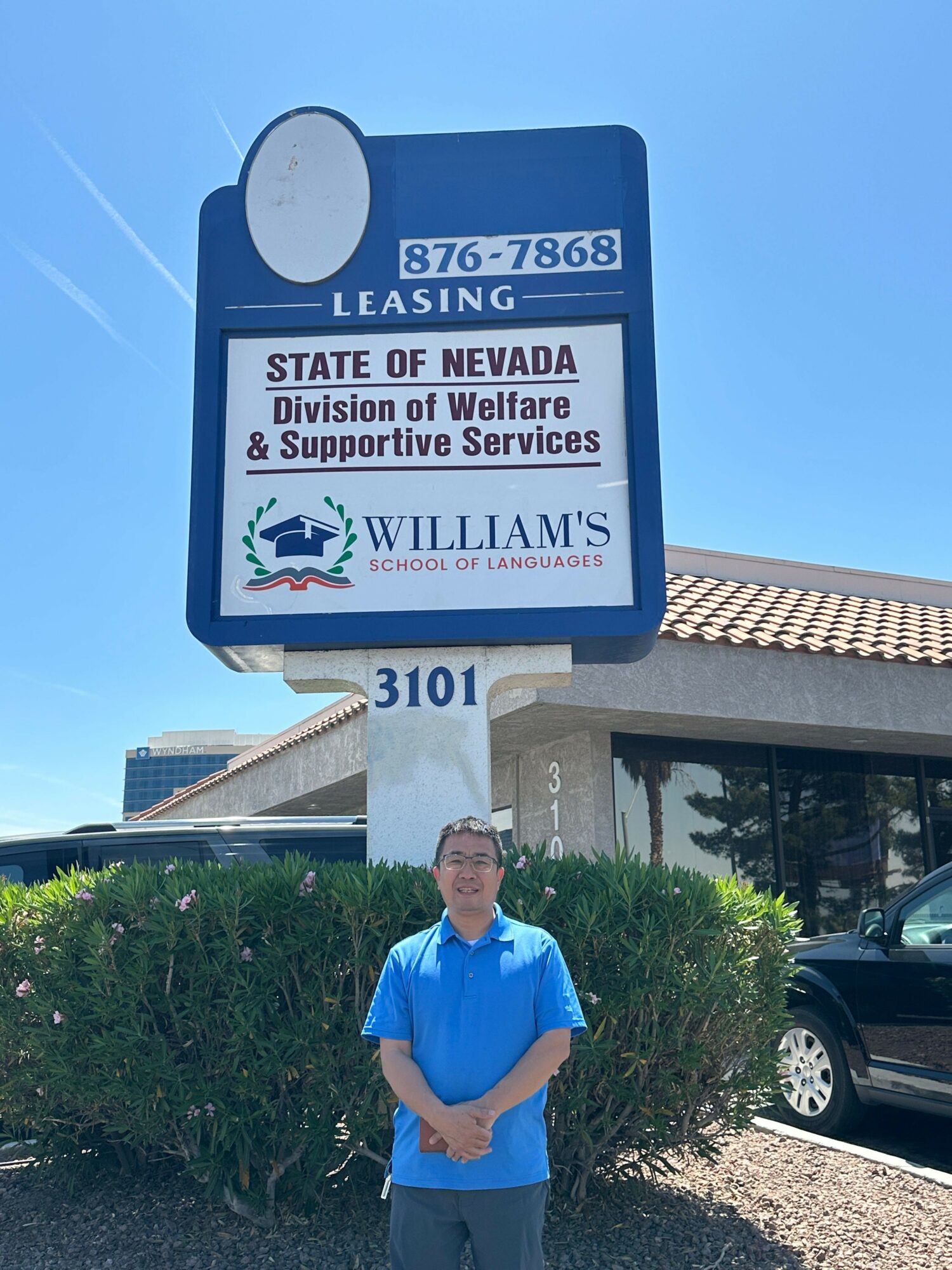 Person in blue scrubs standing outside near a sign for Nevada State of Emergency services, with a building and car in background.