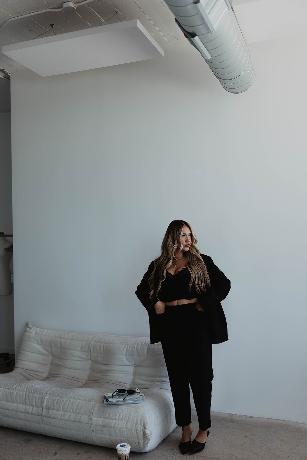 Woman standing in a room with a white sofa, light blue wall, and ceiling duct, looking to the side.