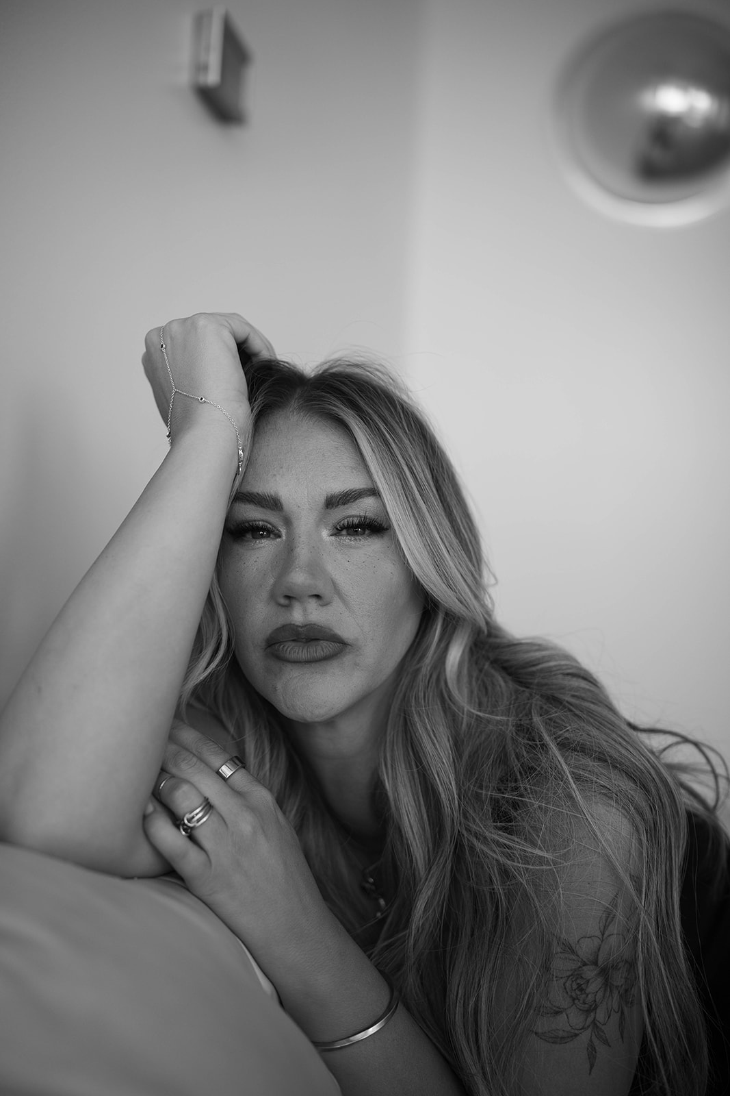 Woman with long hair resting her head on her hand, looking at the camera, in black and white.