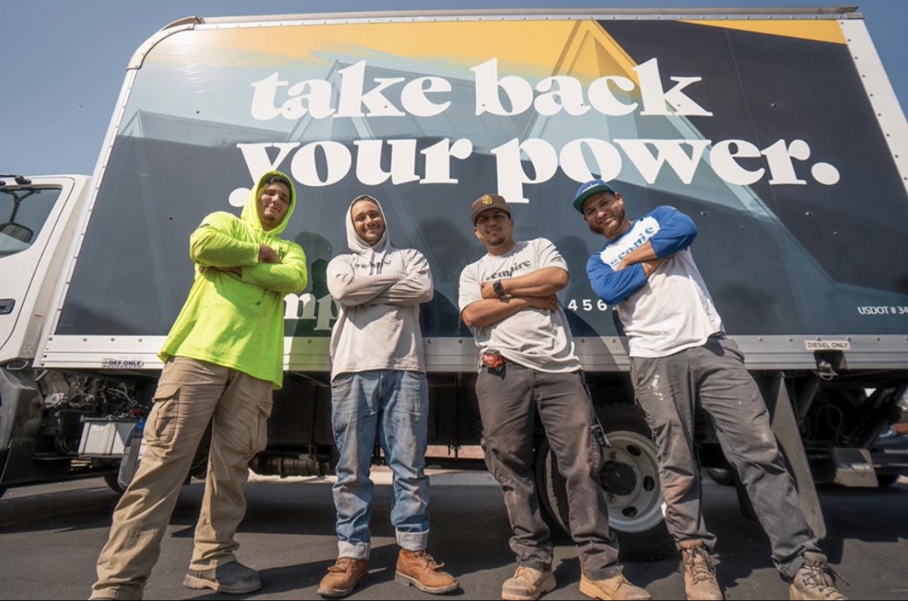 Four people stand in front of a large billboard with the text 